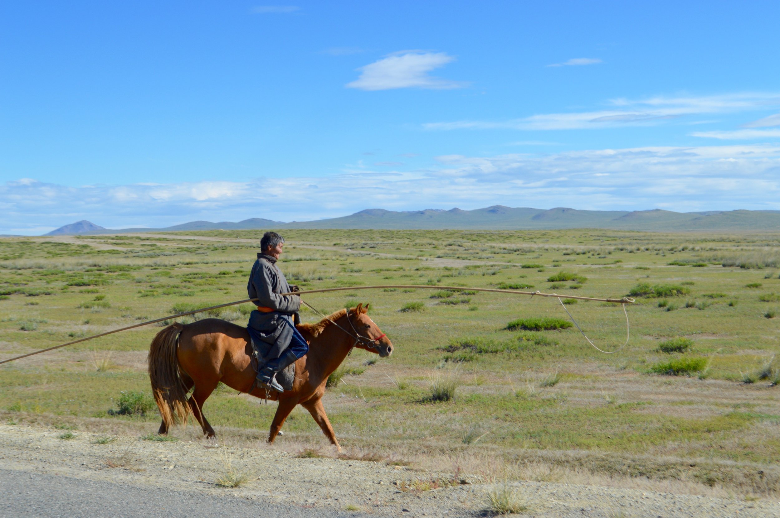 A Mongolian herdsman in traditional clothing on horseback