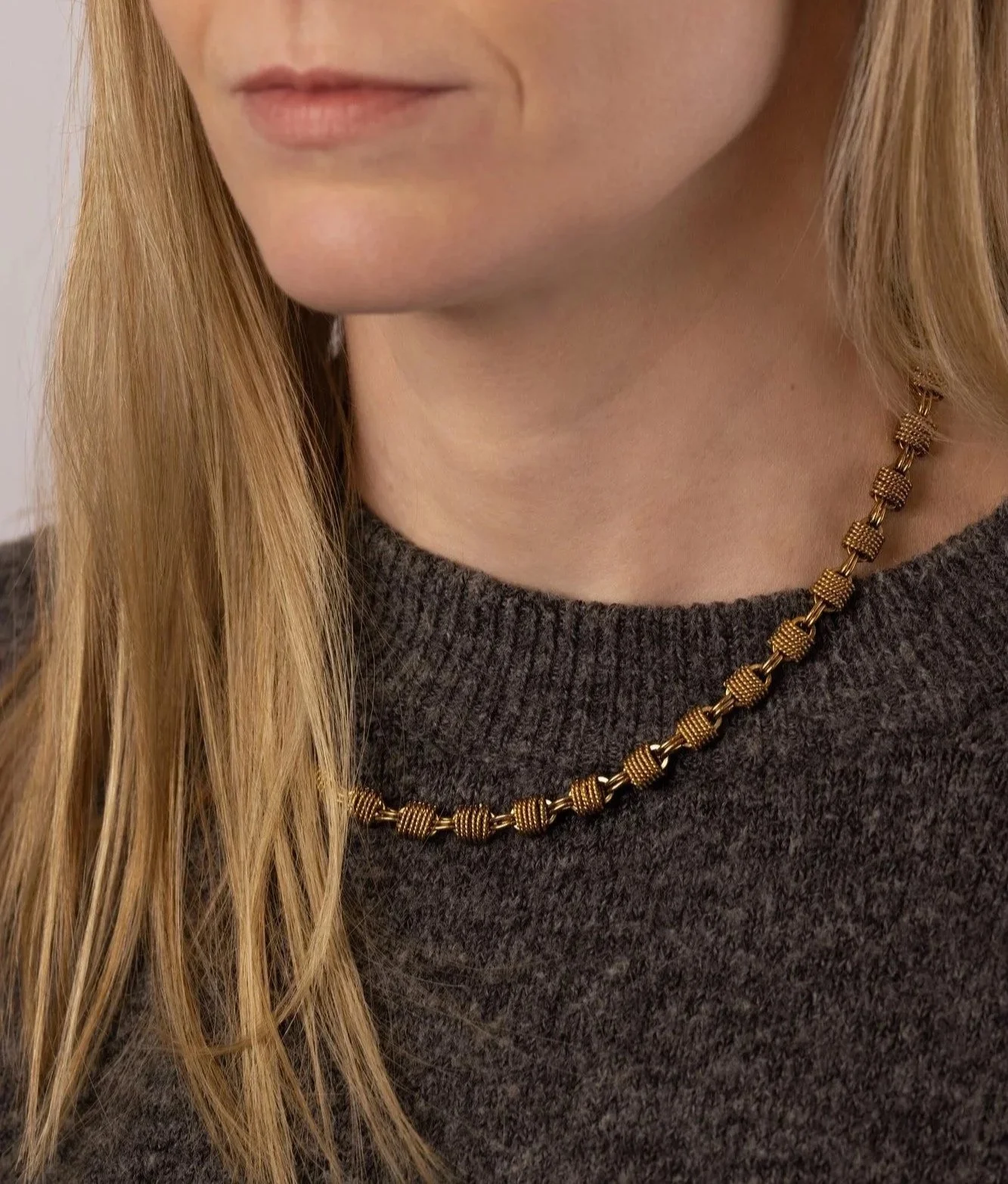 House Thirteen Woven Chunky Chain Necklace worn on model with grey knit jumper. Gold woven link chain necklace