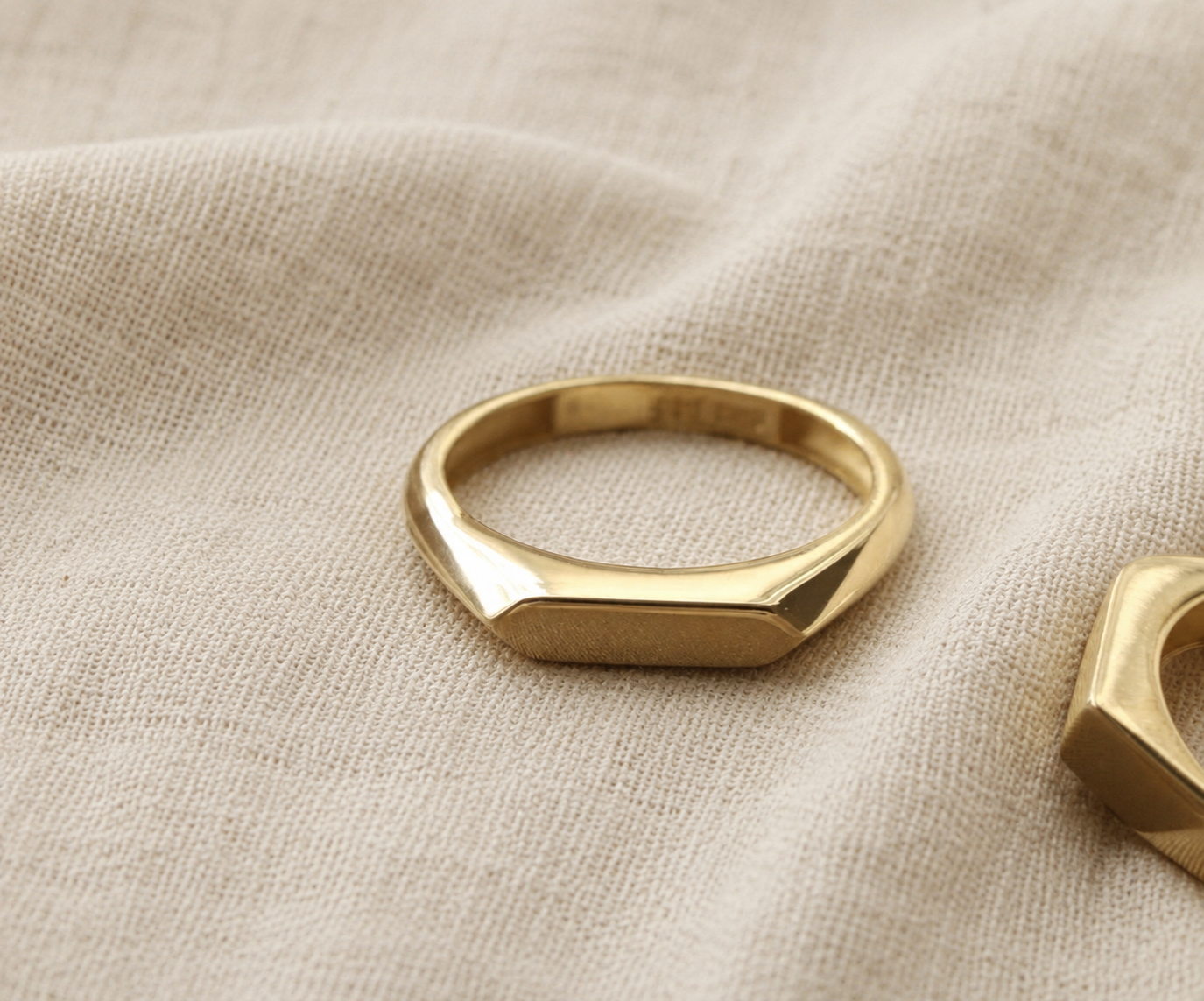 Close-up of slim gold signet ring with geometric faceted edges resting on natural linen fabric