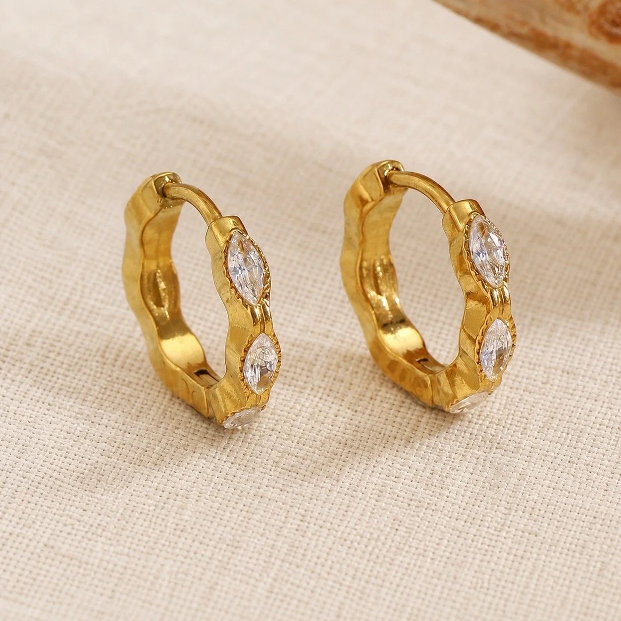 House Thirteen Luna Huggie Earrings styled on cream linen, gold marquise CZ huggie hoop earrings