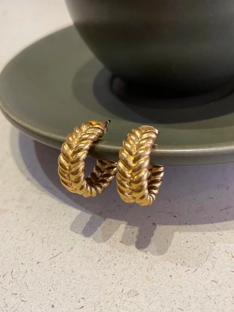 House Thirteen Chunky Braided Hoop Earrings resting on sage green ceramic dish, gold braided texture hoop earrings