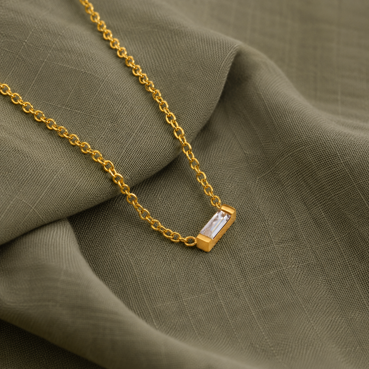 House Thirteen Baguette Necklace. Waterproof gold baguette CZ necklace styled on sage green fabric.