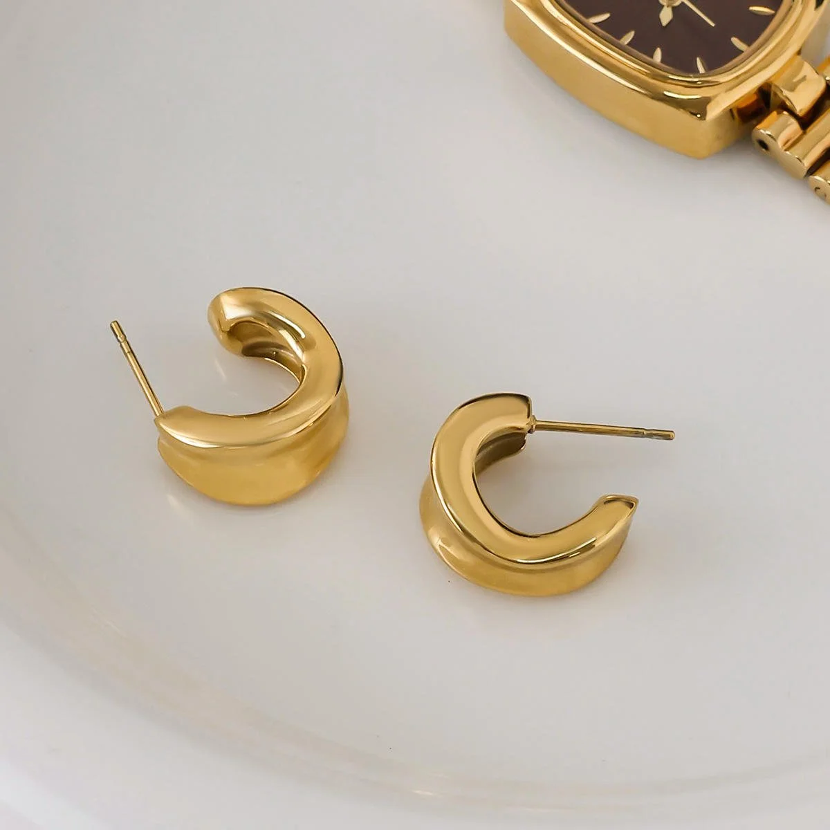 House Thirteen Sculpted Hoop Earrings styled on white ceramic dish with gold watch, waterproof gold chunky hoop earrings