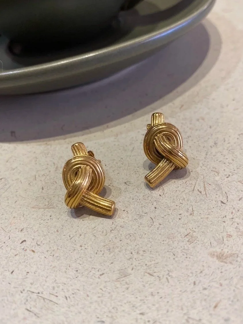 House Thirteen Knot Stud Earrings styled on travertine surface, gold chunky knot stud earrings