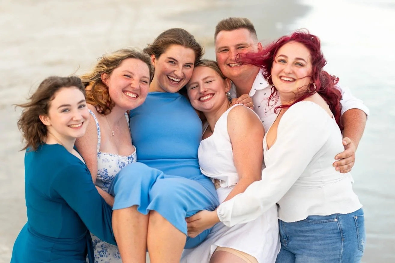 Group of seven friends smiling and hugging each other on the beach