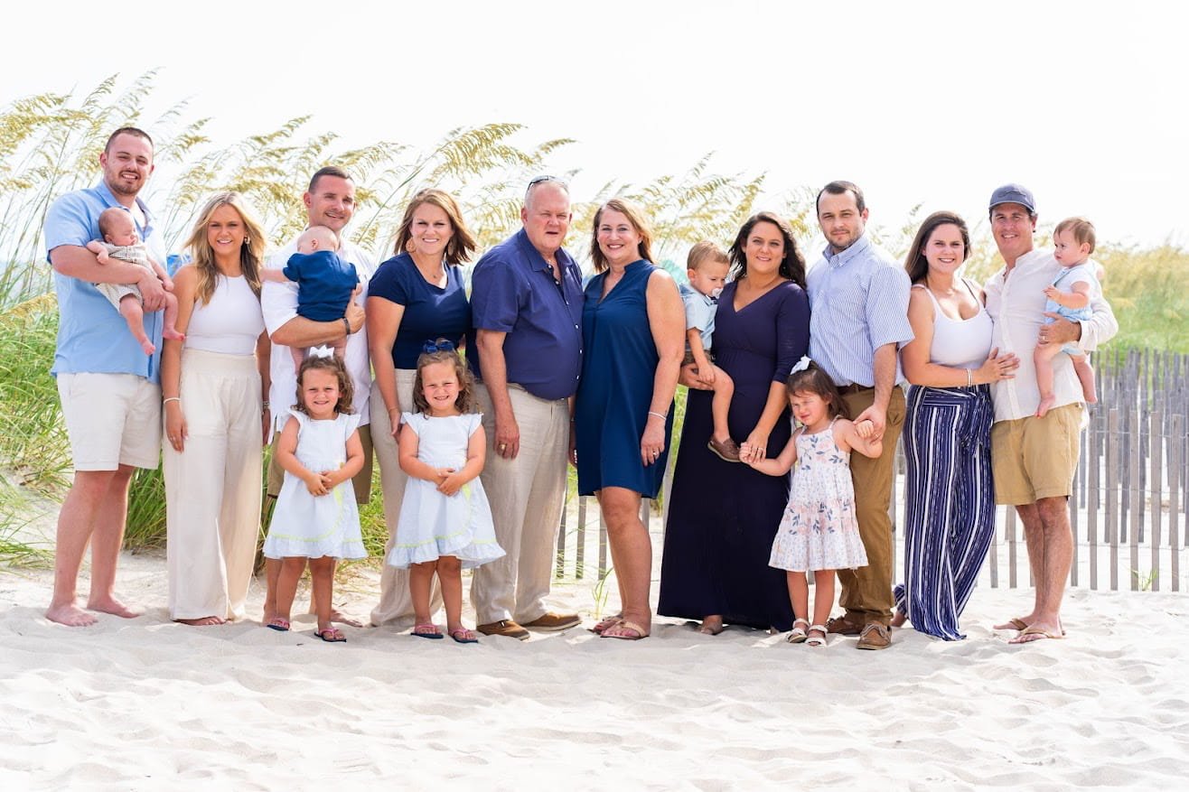 Family gathering on the beach with adults and children smiling and standing together.