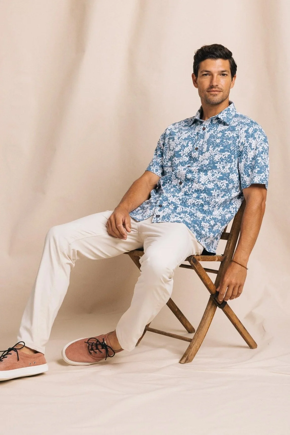 Model Benj Lee sitting in wooden folding chair on fashion set - Southern Tide campaign by Scott Wild