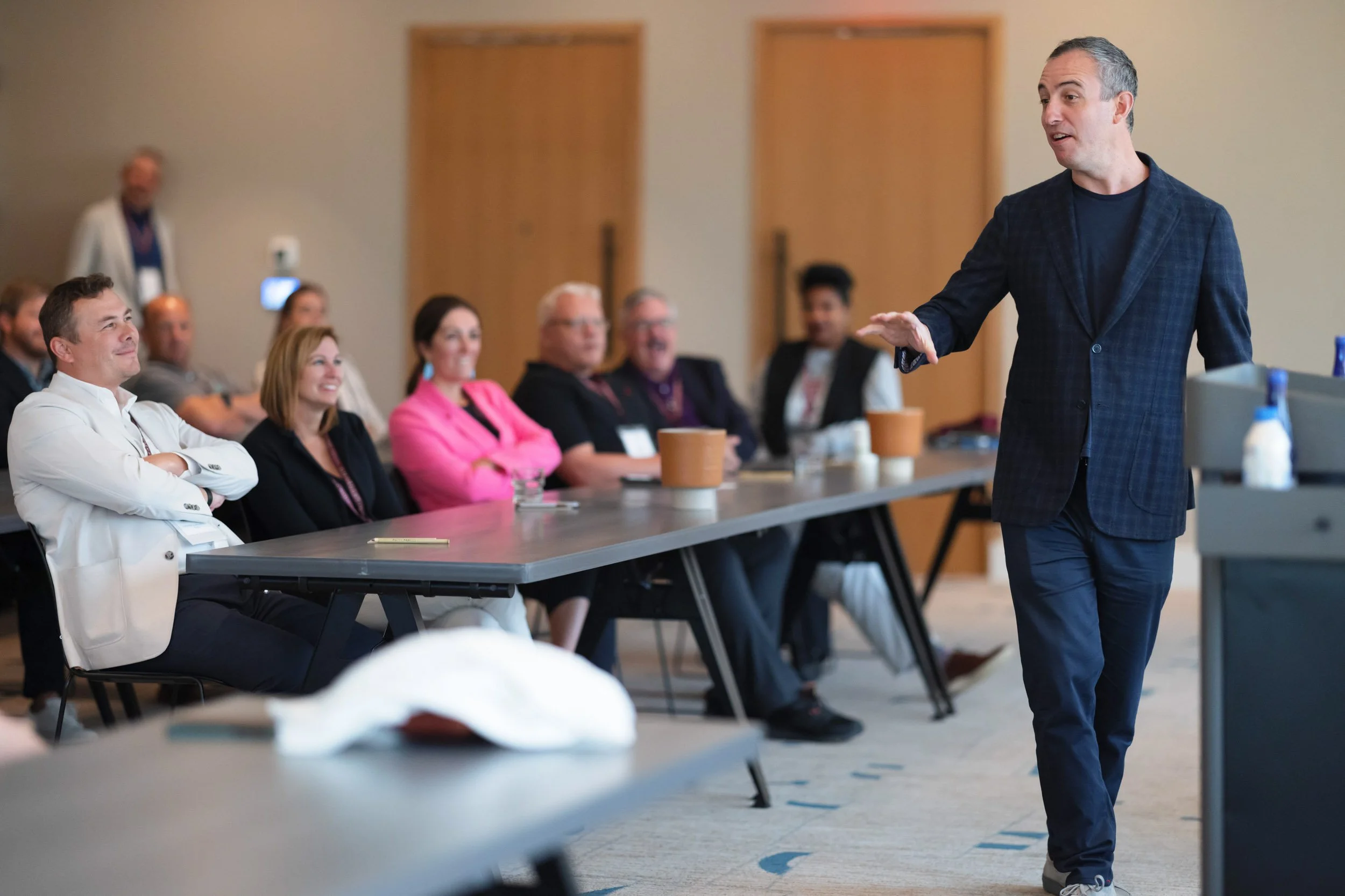 Man on the right speaking to a smiling audience in the Hotel Marcel conference room