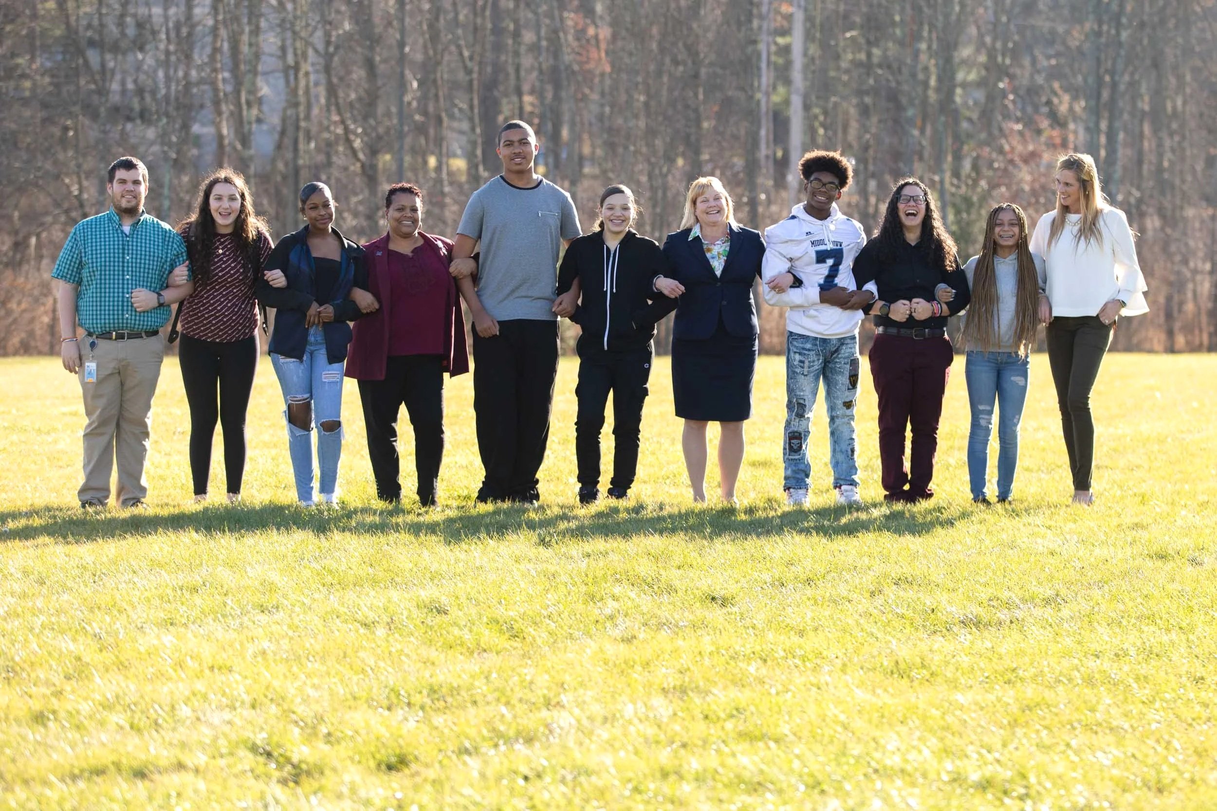 Group shot of 11 Teachers and students locked arm in arm in a field 