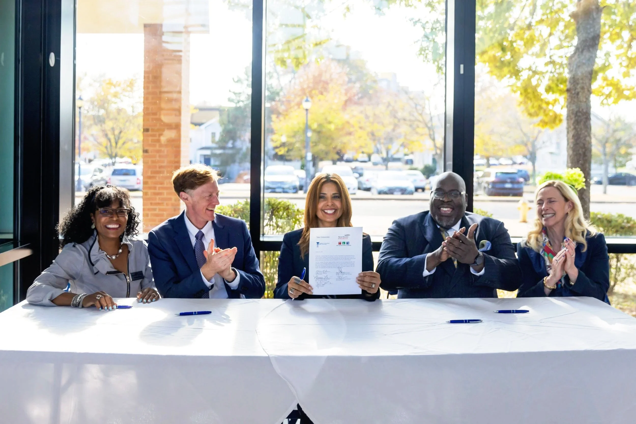 Nonprofit and civic leaders seated at a table holding and signing a formal agreement during a community partnership event in Connecticut.
