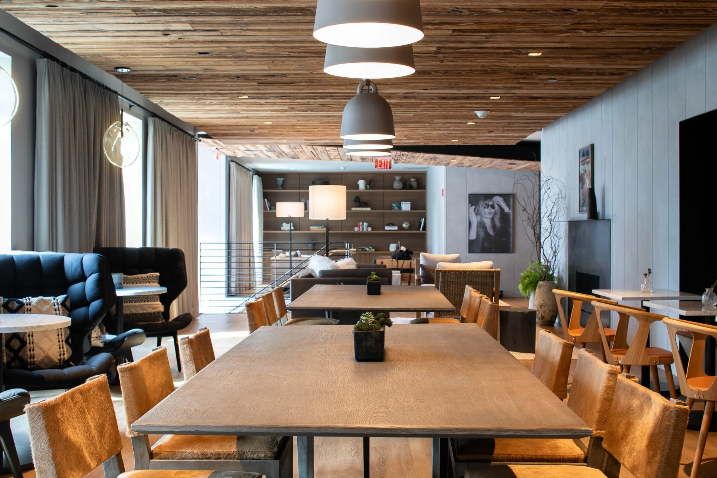Interior photograph of a modern commercial building amenity space with communal tables, warm wood finishes, and contemporary lighting.