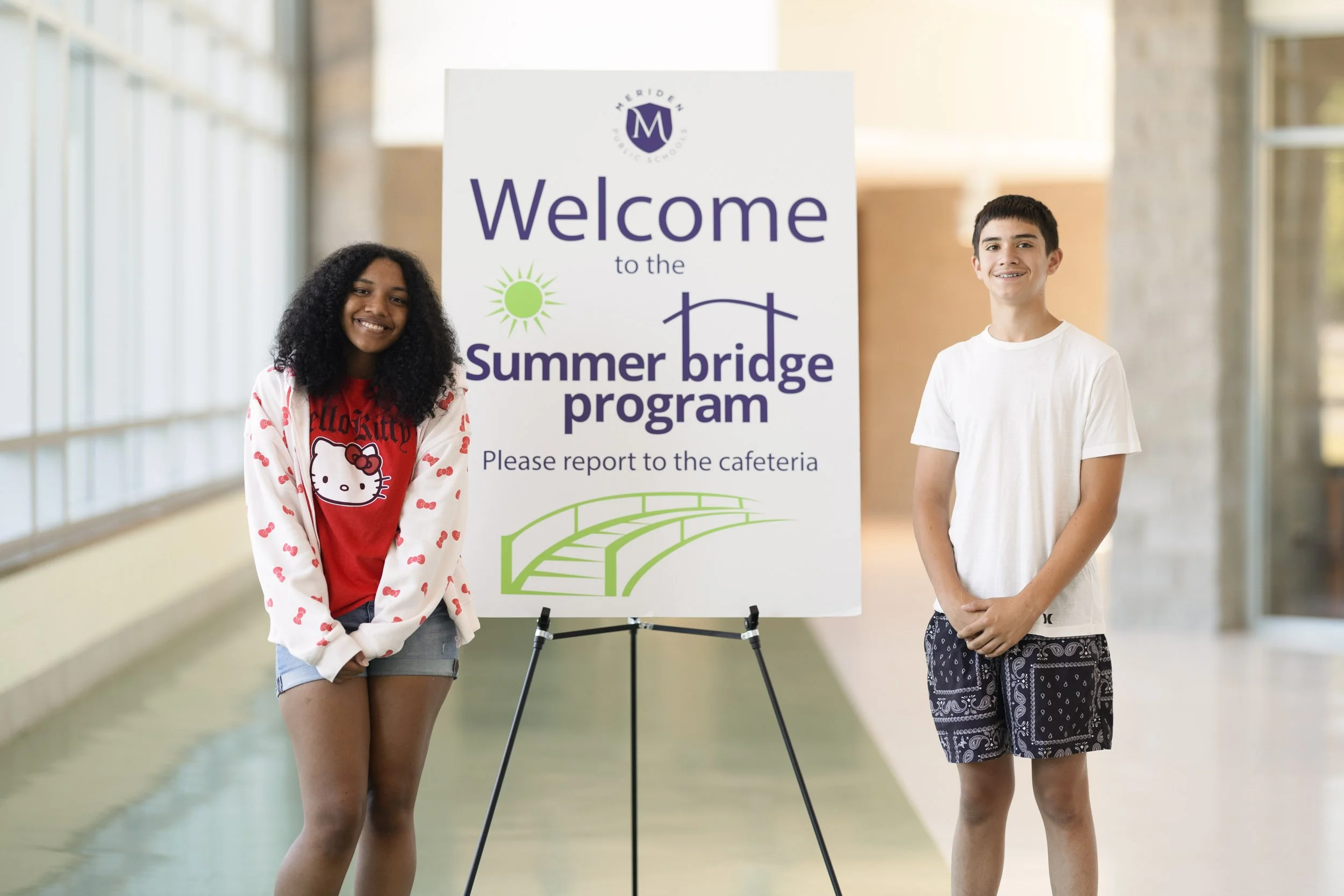 Two students standing next to a welcome sign for a summer school program