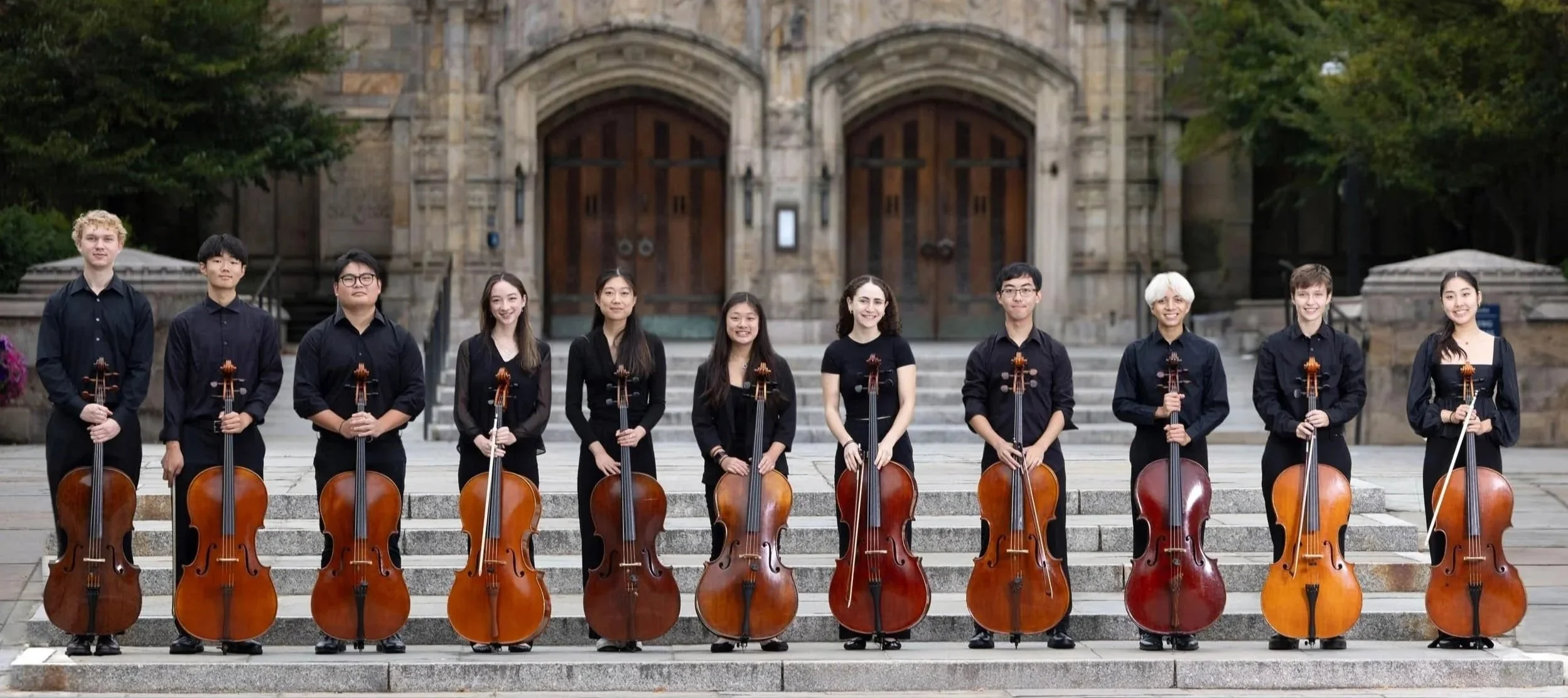 College student cellists posing together with their instruments outside an academic building