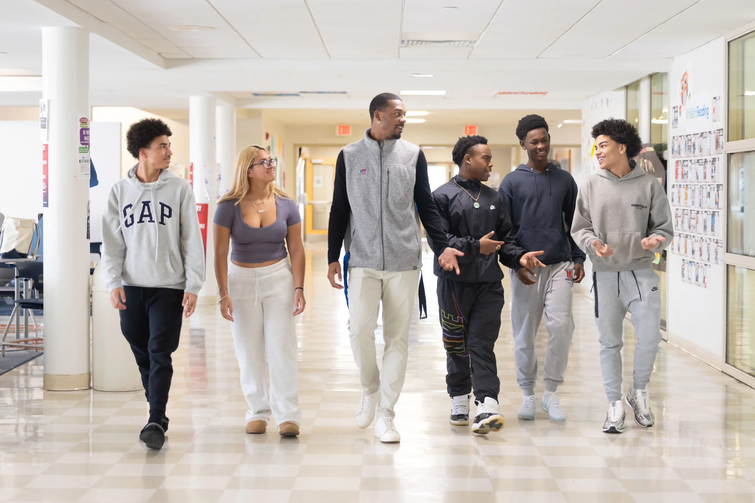 A teacher with five students walking down the hall and smiling