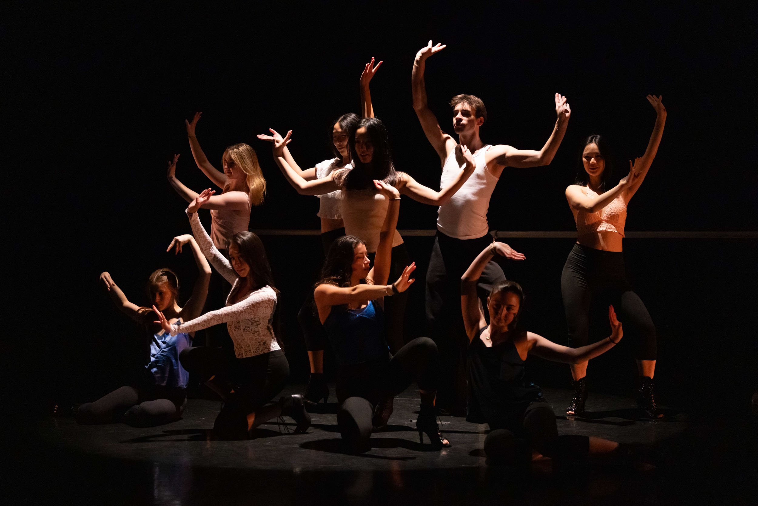 A full ensemble moves in unison under theatrical light, arms lifted and folded into precise shapes. The image captures the discipline, timing, and collective energy that define contemporary dance onstage.