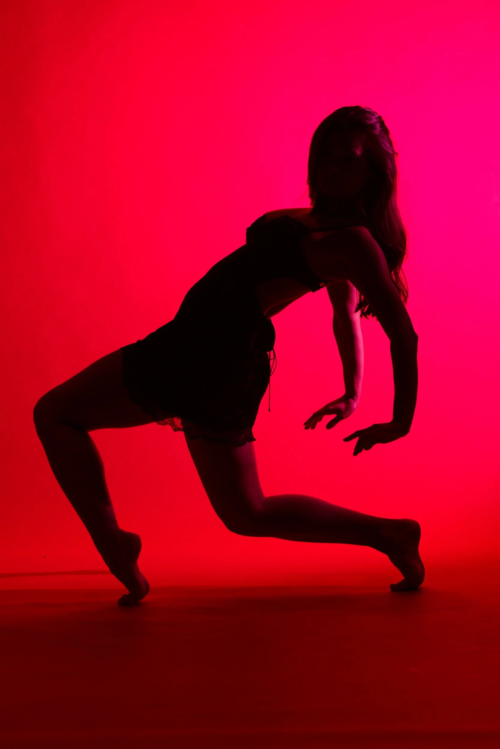 A dancer moves through shadow and saturated color, her form defined by light and motion. The image focuses on shape, line, and the physical language of dance.