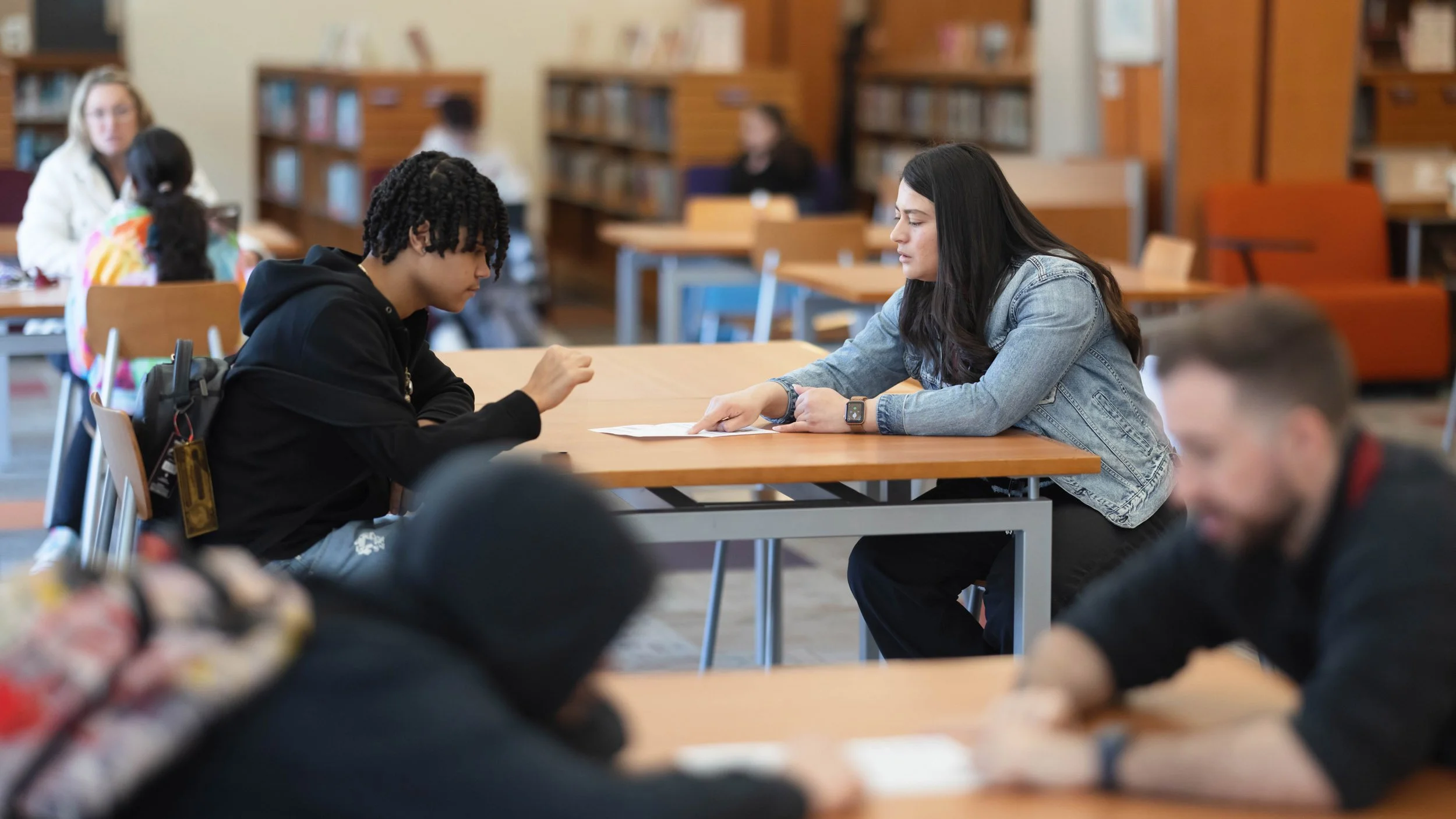 Student and educator meeting at a table in a school library, reviewing documents during an academic support session in Connecticut.