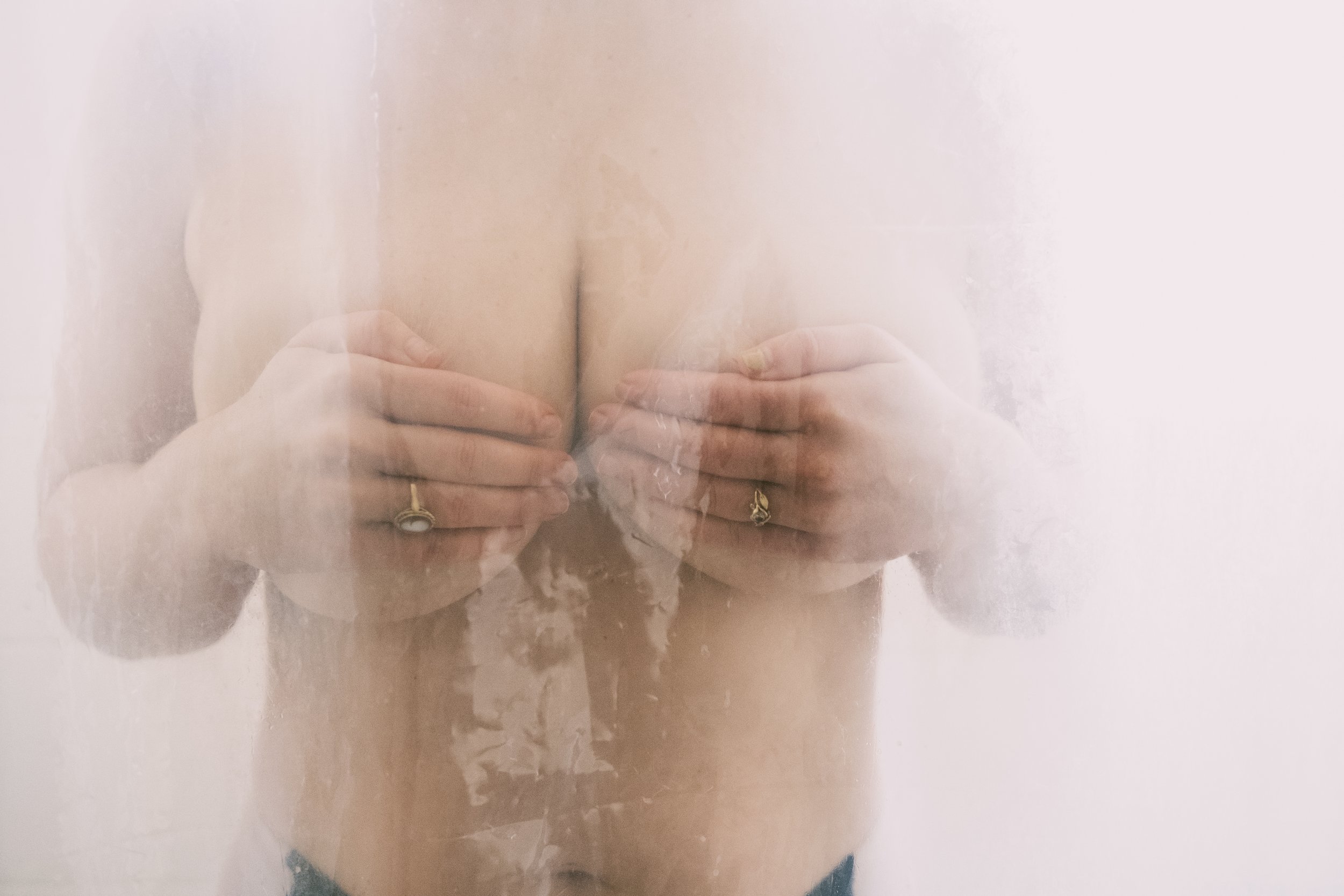 A person holding their chest with both hands, with reflections on a mirror creating multiple images of the hands and chest.