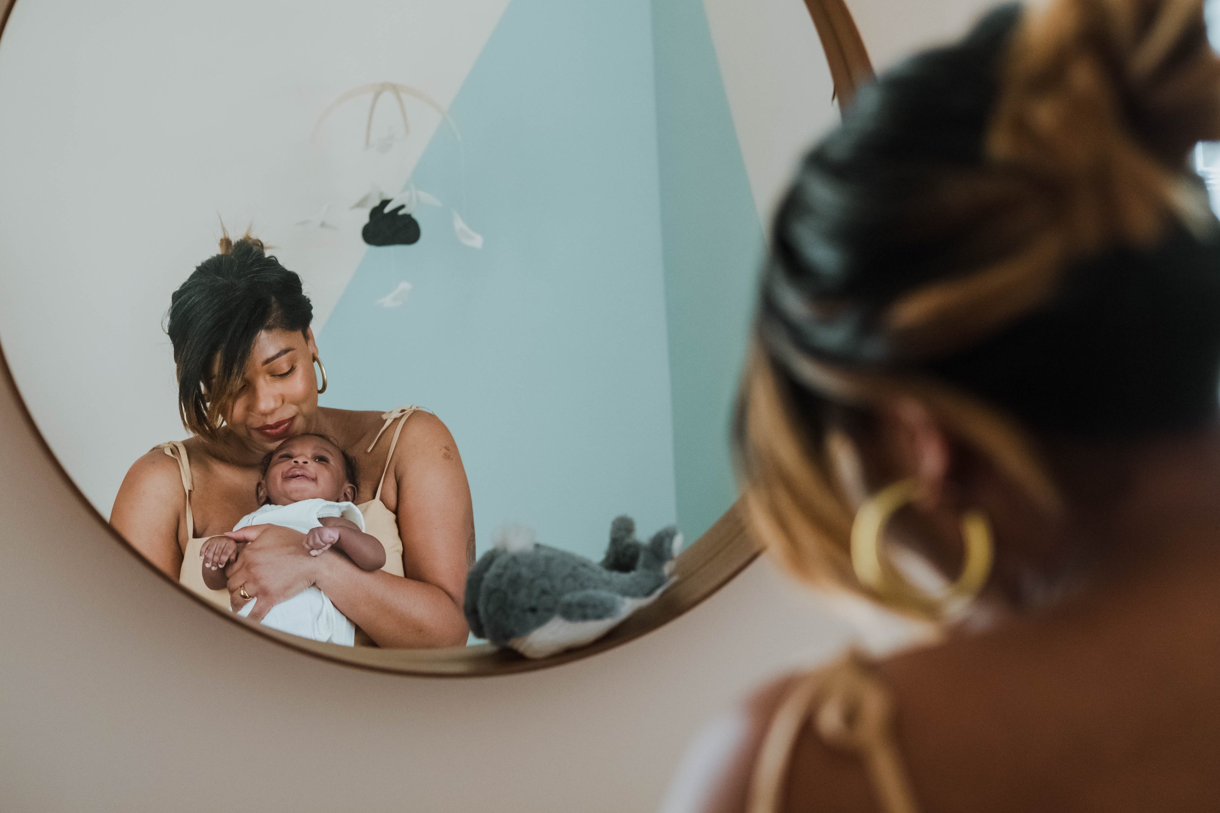 A woman with dark hair and hoop earrings holding a smiling baby, reflected in a mirror.