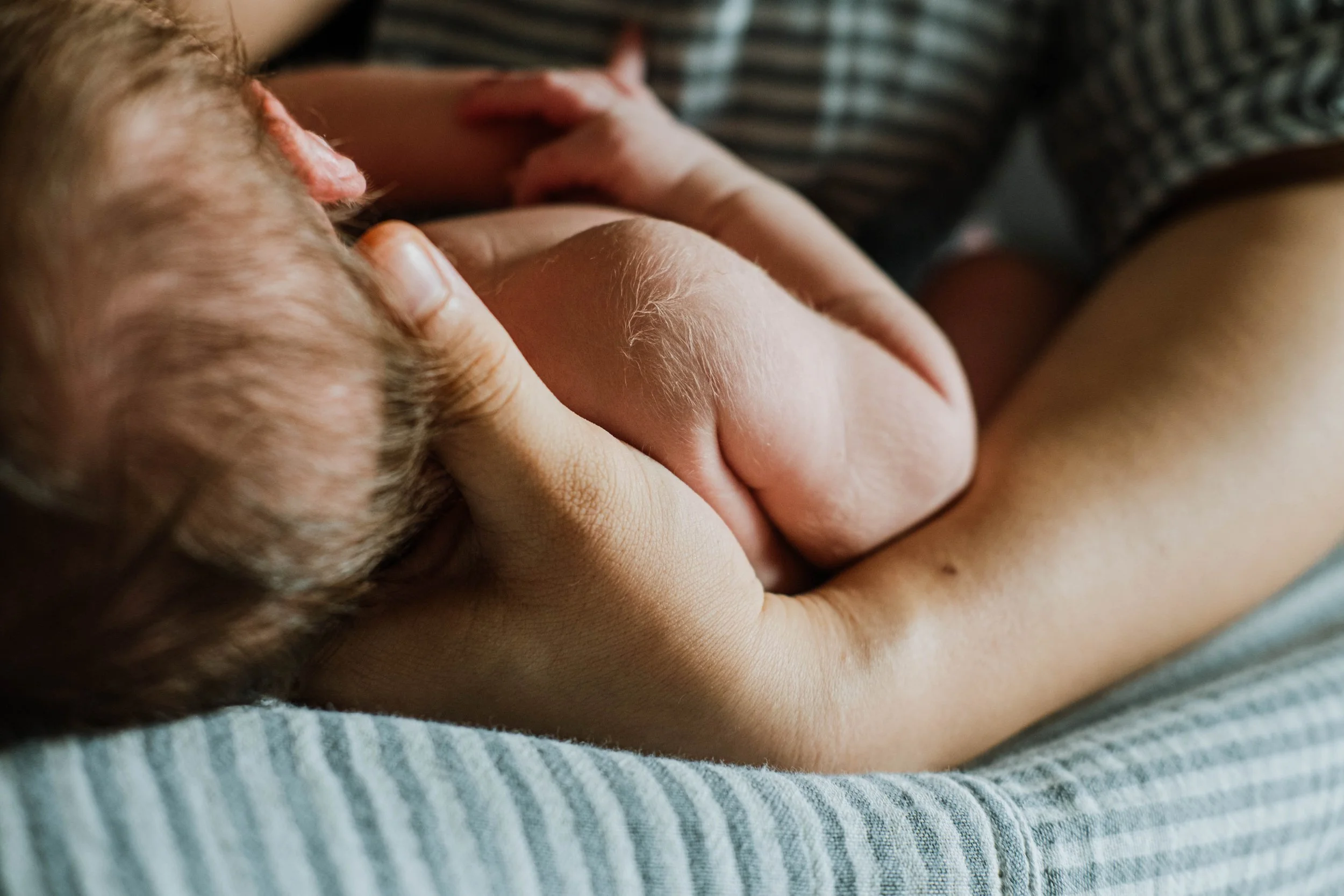 Close-up of a person breastfeeding a baby, showing the baby's face and mother's hand gently holding the baby.