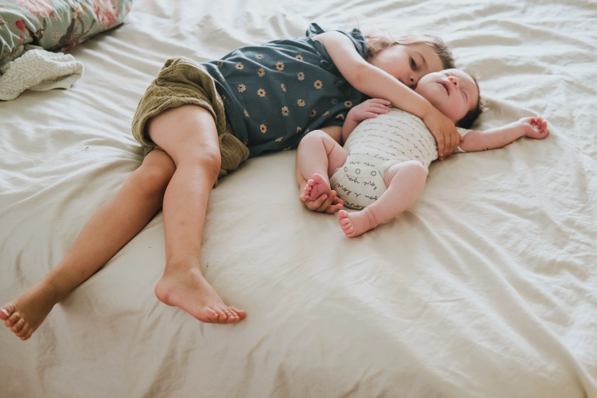 Two children, a boy and a baby, lying on a bed together. The boy is hugging the baby, and they are both sleeping.