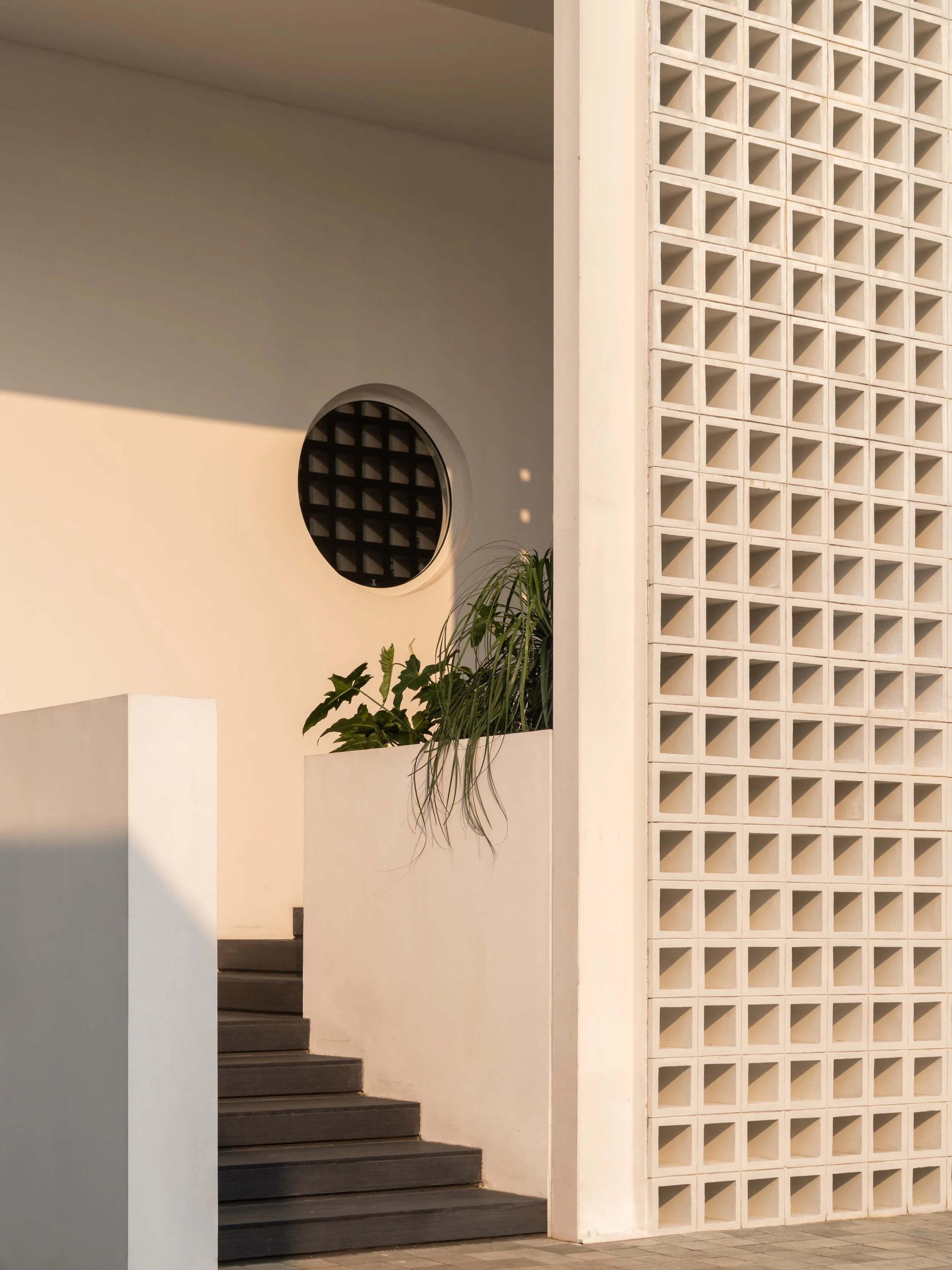 Jakarta Courtyard House

The house is entered from the inner courtyard, up a short flight of steps concealed behind a screen of square concrete blocks and a planter, adding another layer of privacy.
A circular window offers a glimpse into the inner r