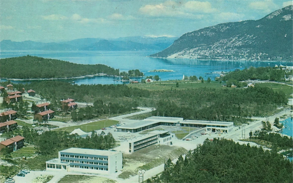 Dette biletet viser Husnes sentrum i 1970. Vi ser SØRAL sitt hybelhus, motellet og det første butikksenteret, som oslofirmaet J. B. Bakke AS bygde i 1967.