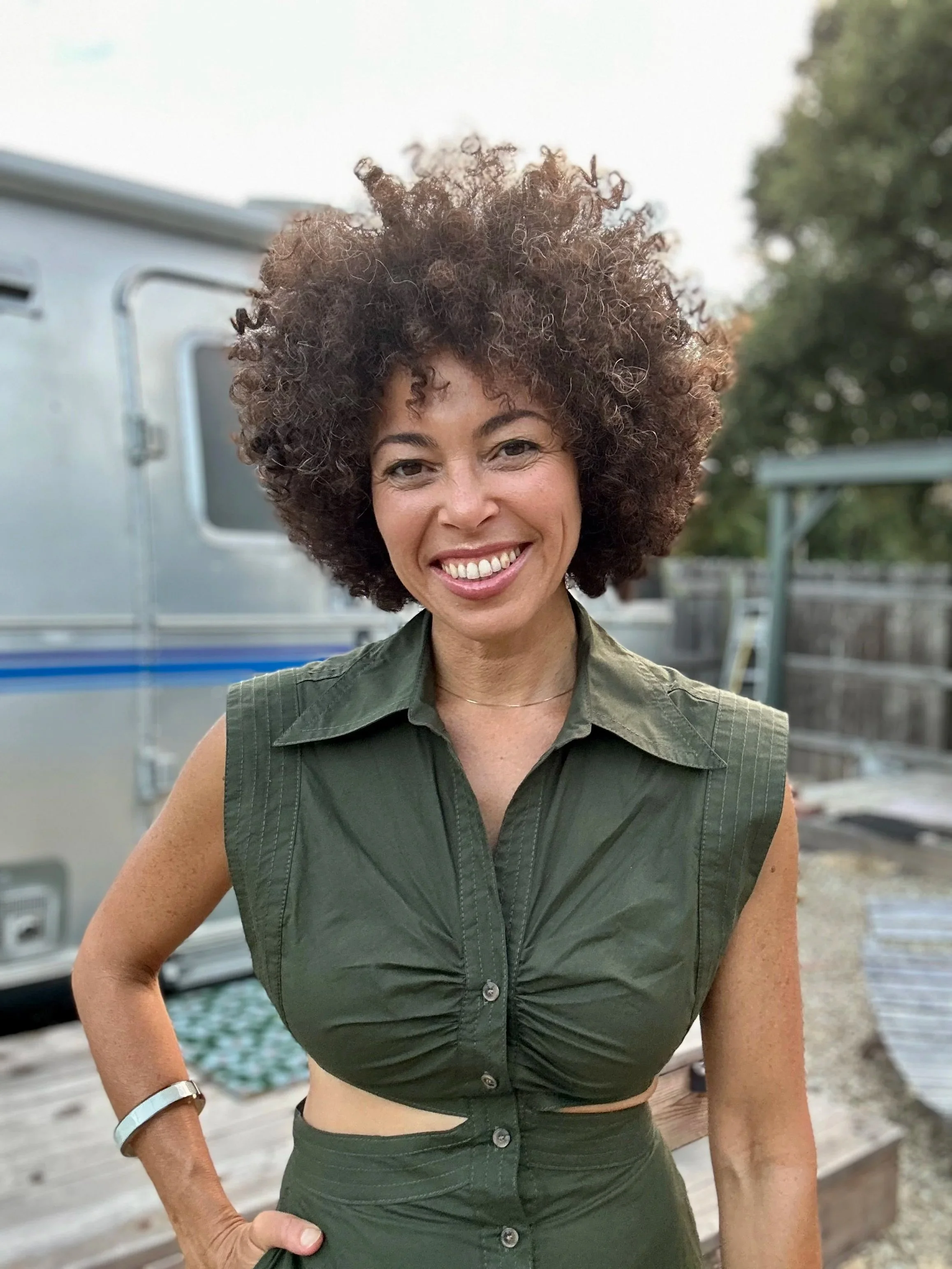 We should feel at home in our lives. Alisha Westerman in a green dress in front of an Airstream trailer under an open sky.