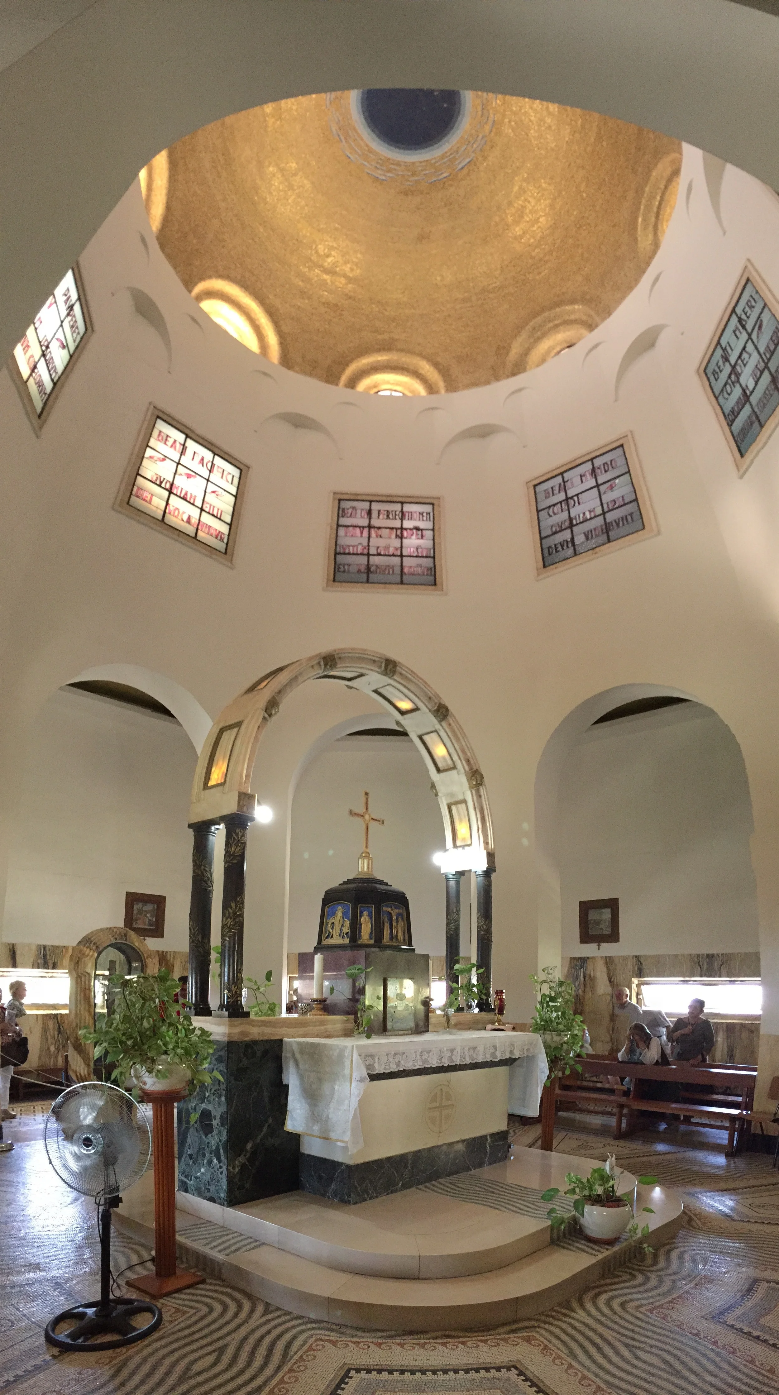 The sanctuary and altar of the church. Golden tiles line the dome roof, and the beatitudes are written in Latin in the upper colored-glass windows.