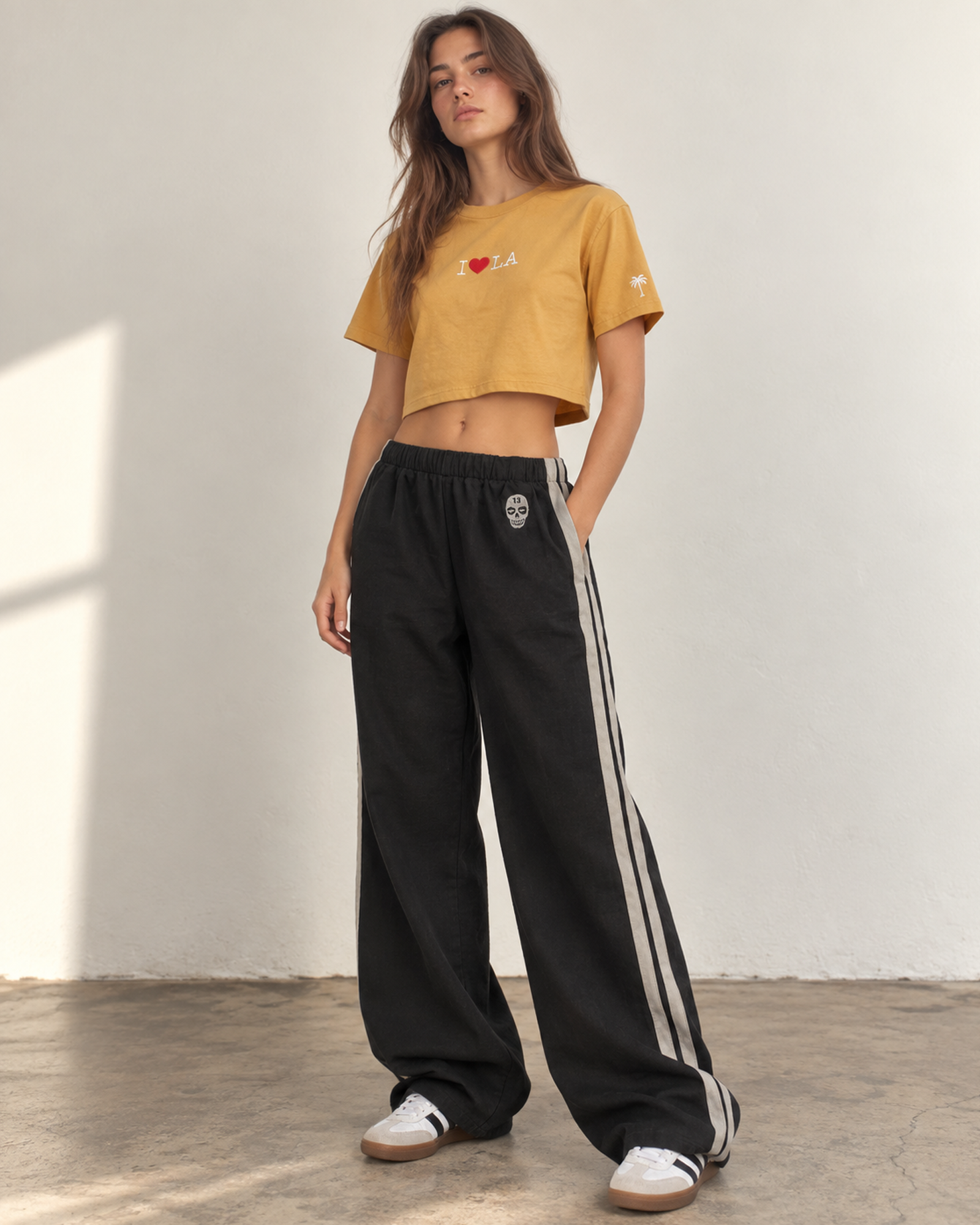 Woman wearing The SellOut black cotton-linen wide-leg track pants with double light-gray side tape and 13 Skull embroidery.