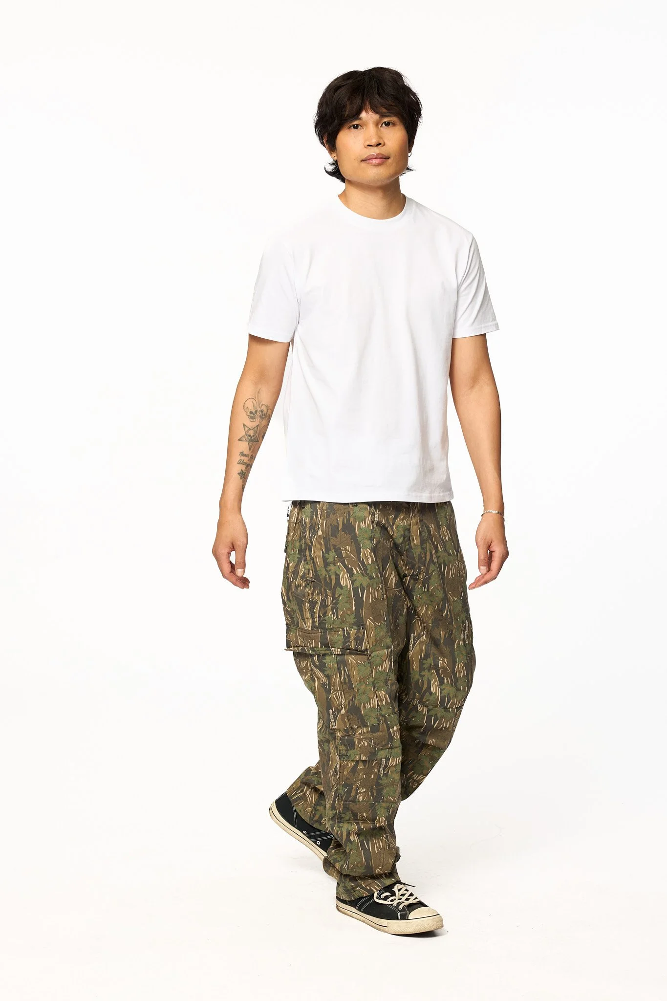 Model wearing The SellOut Heavyweight Short Cut Tee in white styled with camouflage cargo pants in a full body studio photo.
