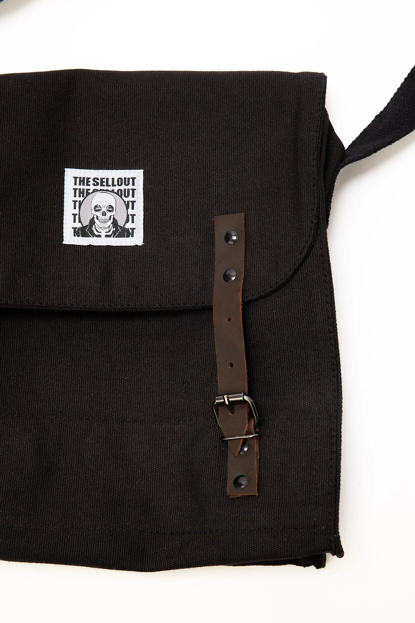 Black canvas shoulder bag close-up showing buckle straps stitching and logo patch detail
