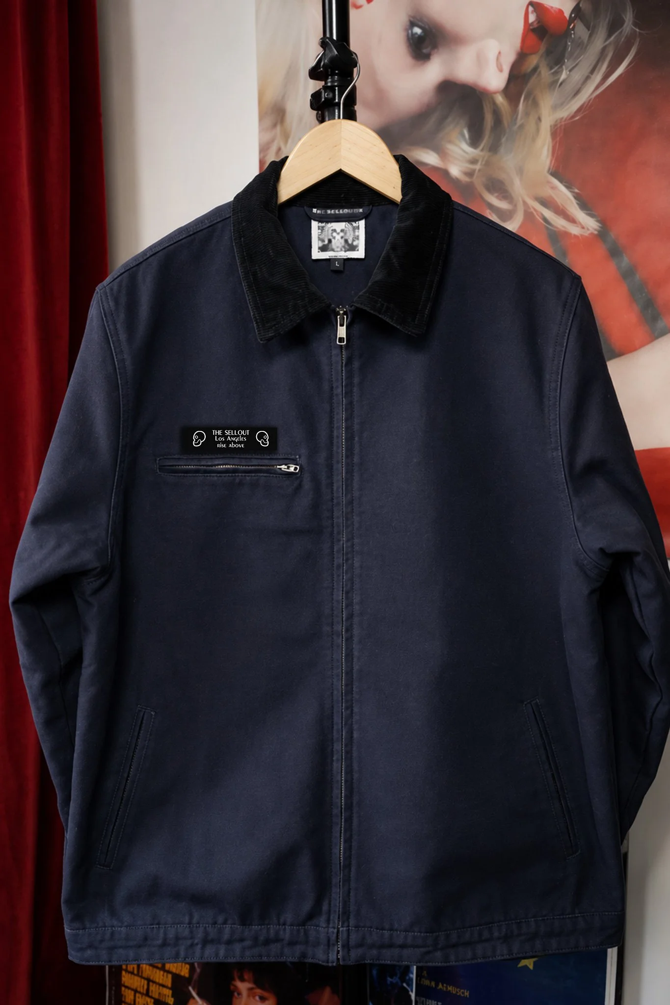 The SellOut navy canvas collar jacket with black corduroy collar hanging on a wooden hanger, front view.