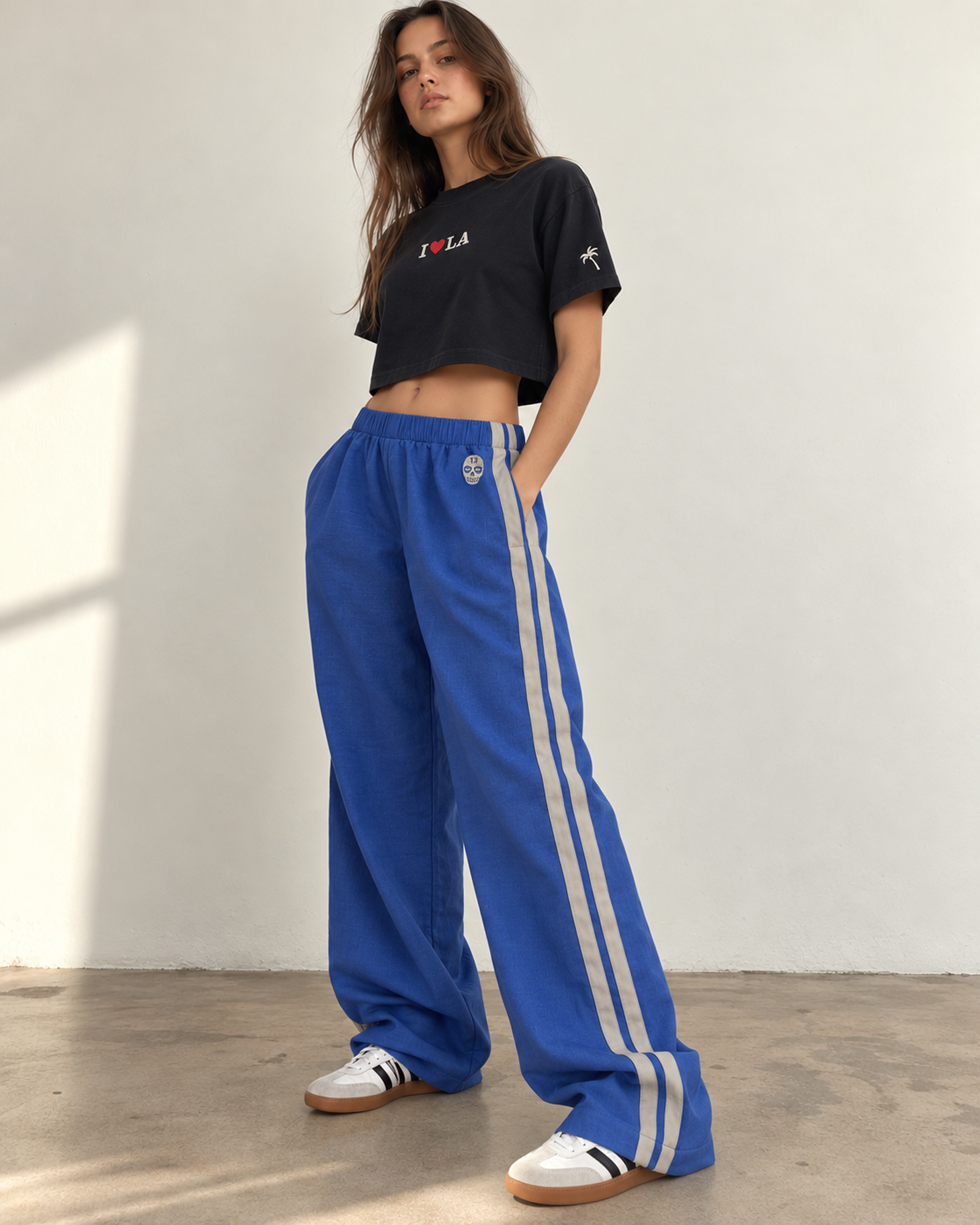 Woman wearing The SellOut blue cotton-linen wide-leg track pants with double light-gray side tape and 13 Skull embroidery.