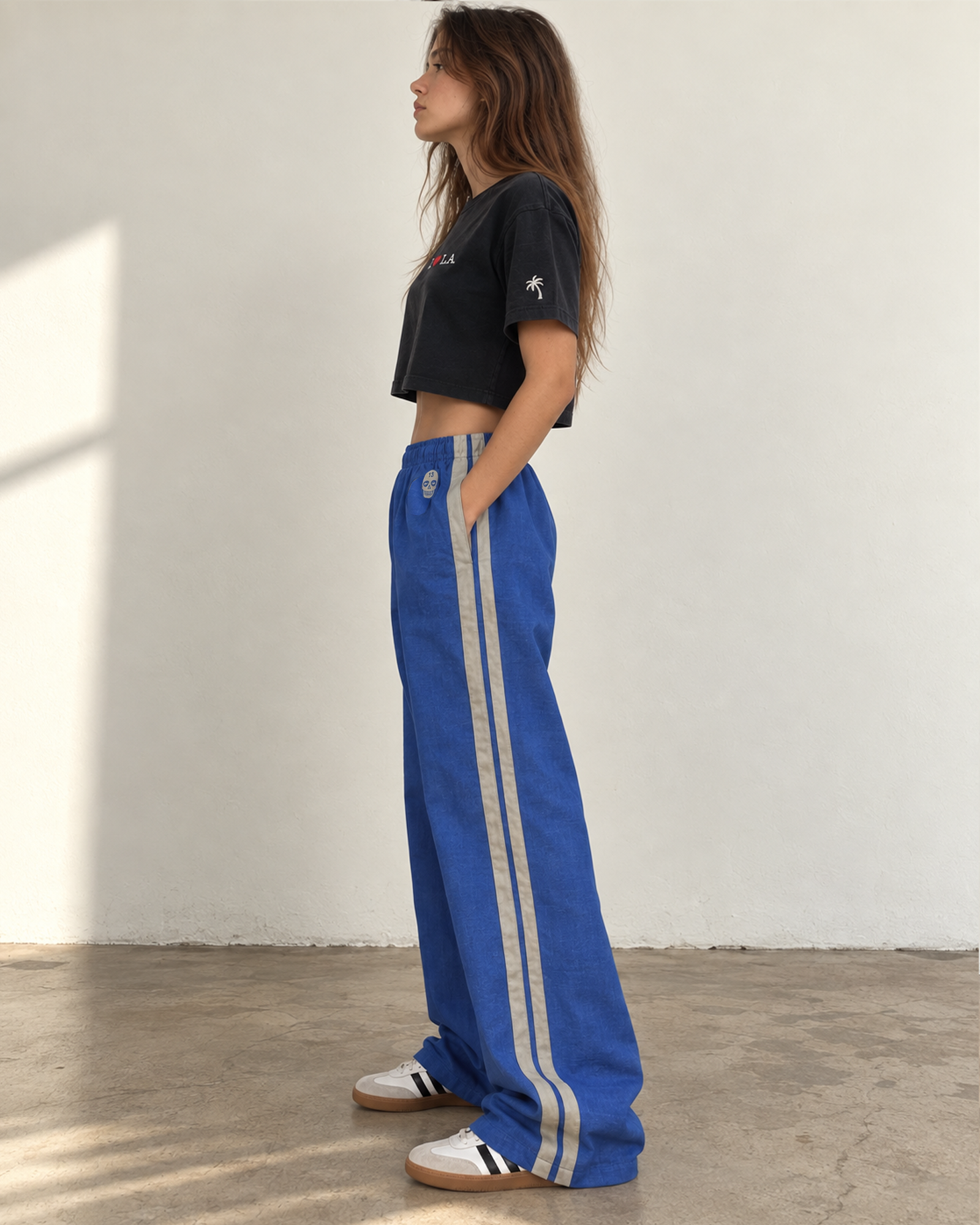 Side view of The SellOut blue cotton-linen wide-leg track pants with double light-gray side tape and 13 Skull embroidery.