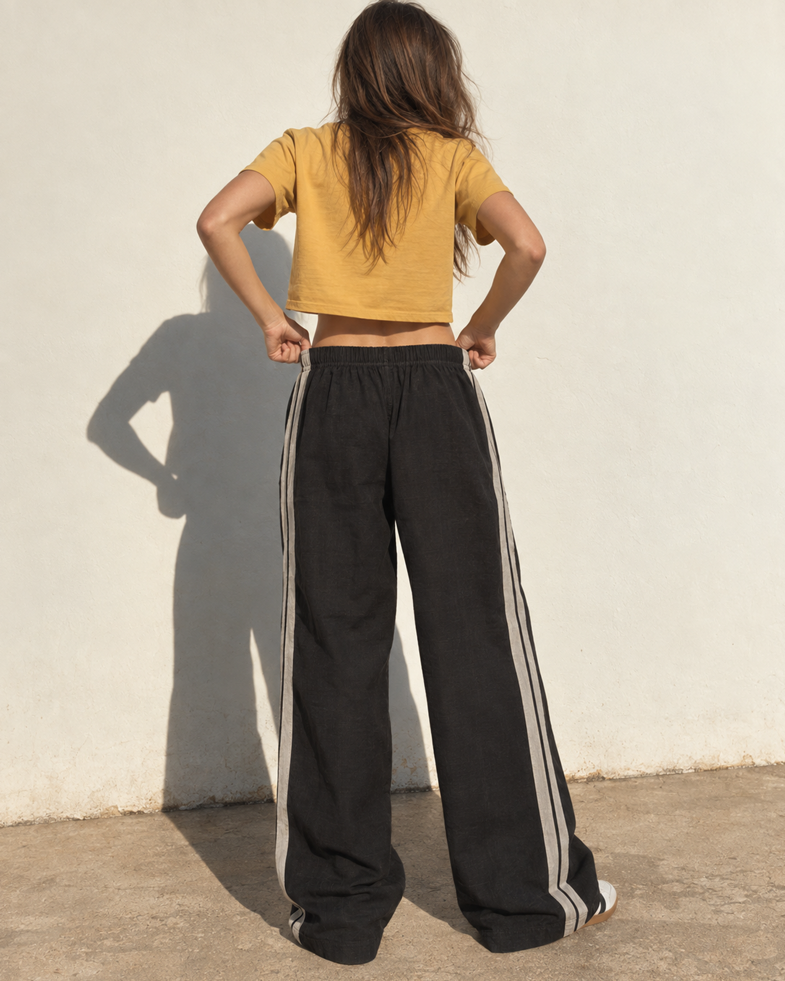Back view of The SellOut black cotton-linen wide-leg track pants with double light-gray side tape outdoors.