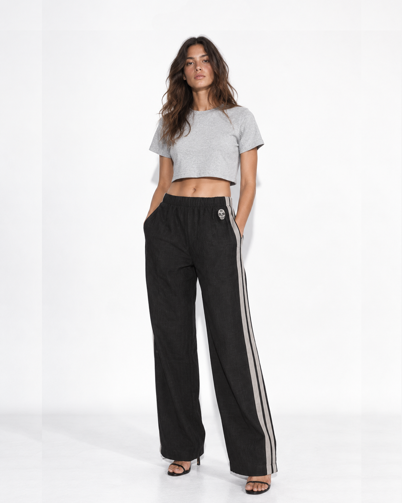 Woman wearing The SellOut black cotton-linen wide-leg track pants with double light-gray side tape and 13 Skull embroidery.