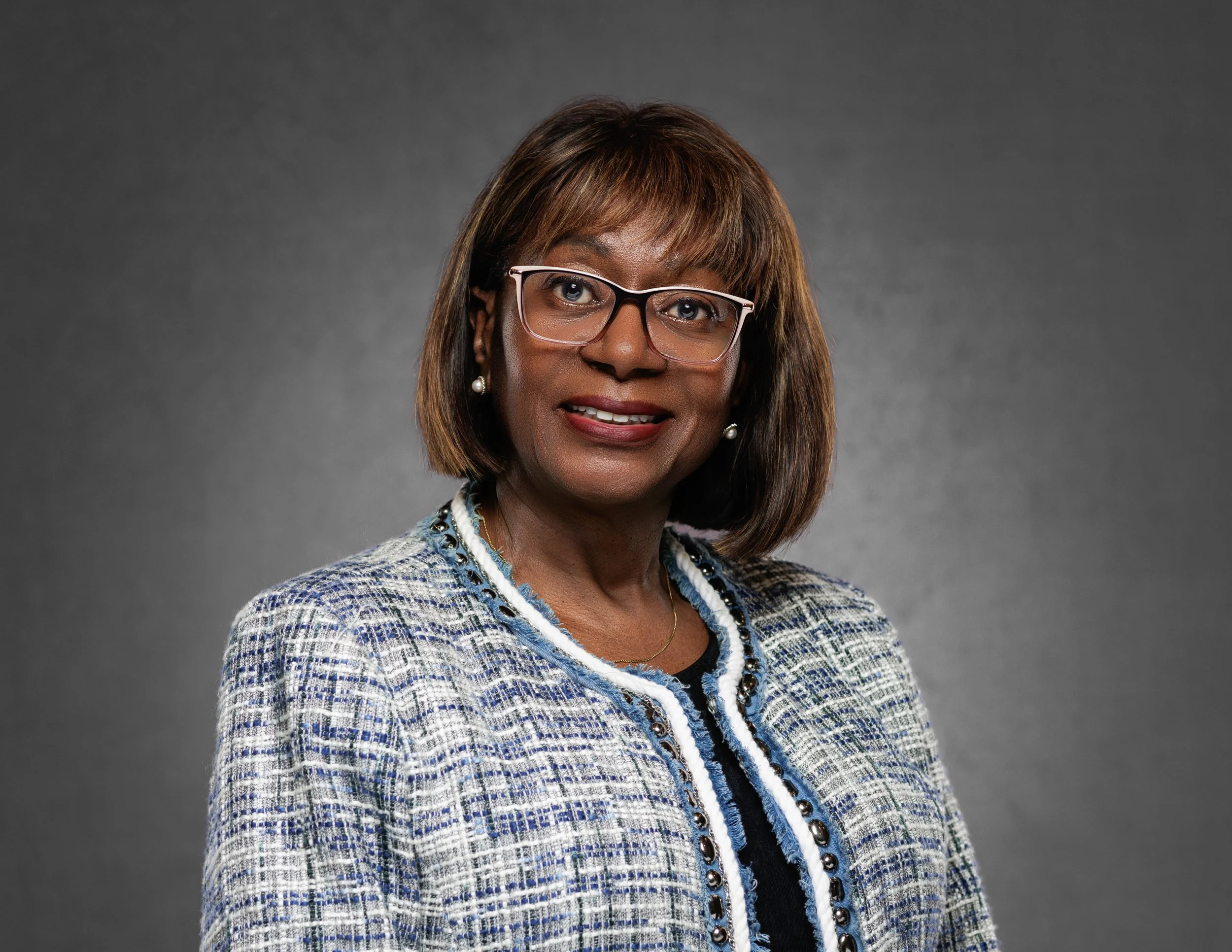 A woman professional headshot standing off camera position with glasses on and a gray background.