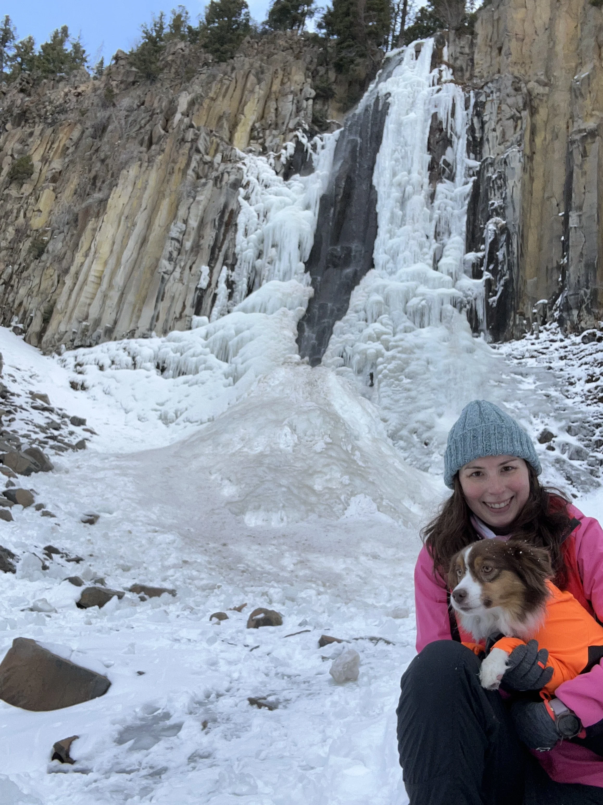 Katie holding her dog in front of a frozen waterfall