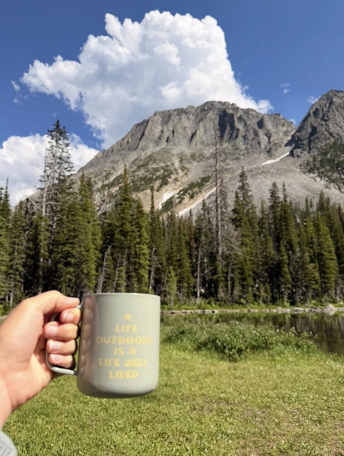 A cup reading A life outdoors is a life well lived in front of a mountain