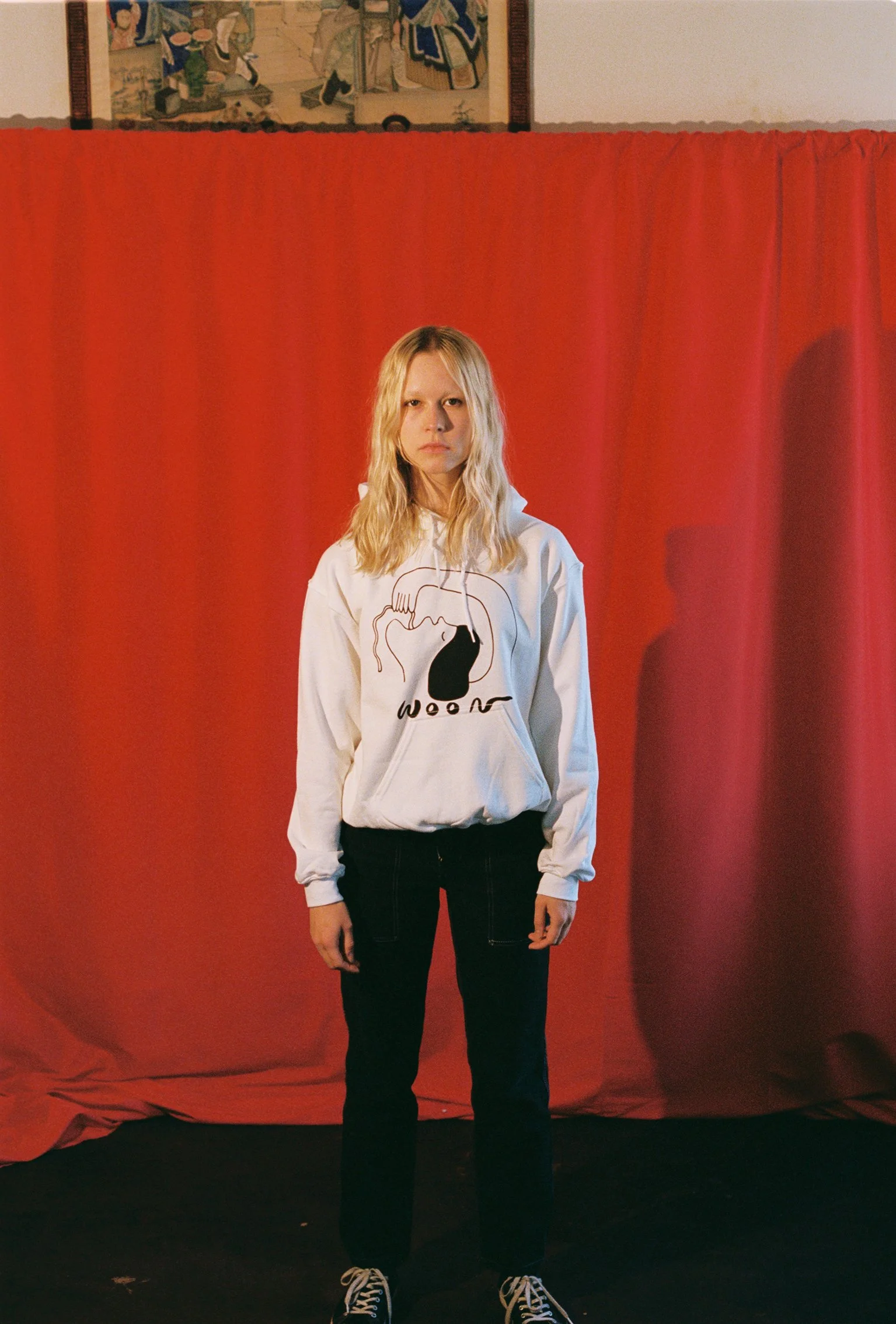 A person wearing a white hoodie with black artwork of a person eating a noodle