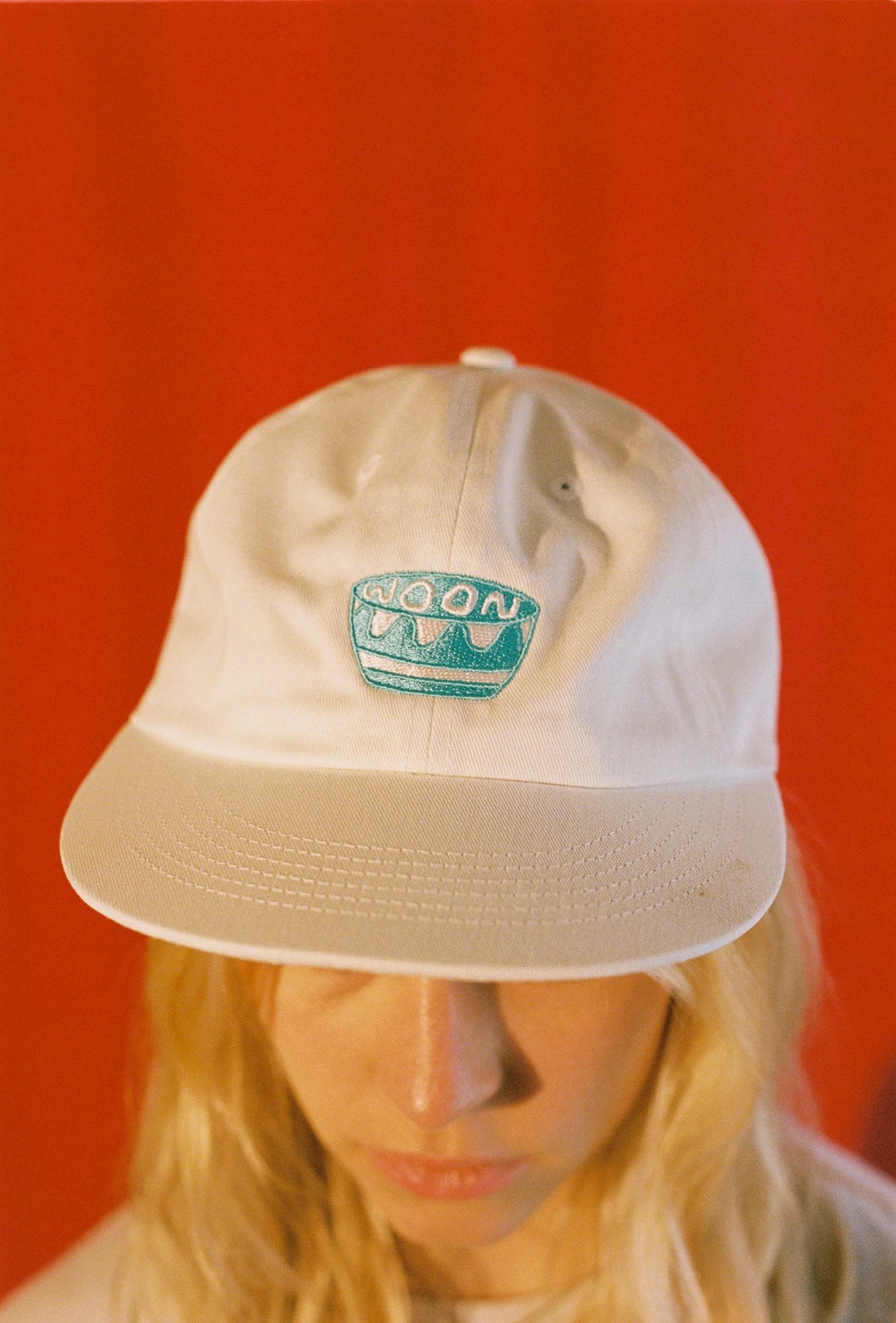 A person wearing a white flat bill cap with blue artwork
