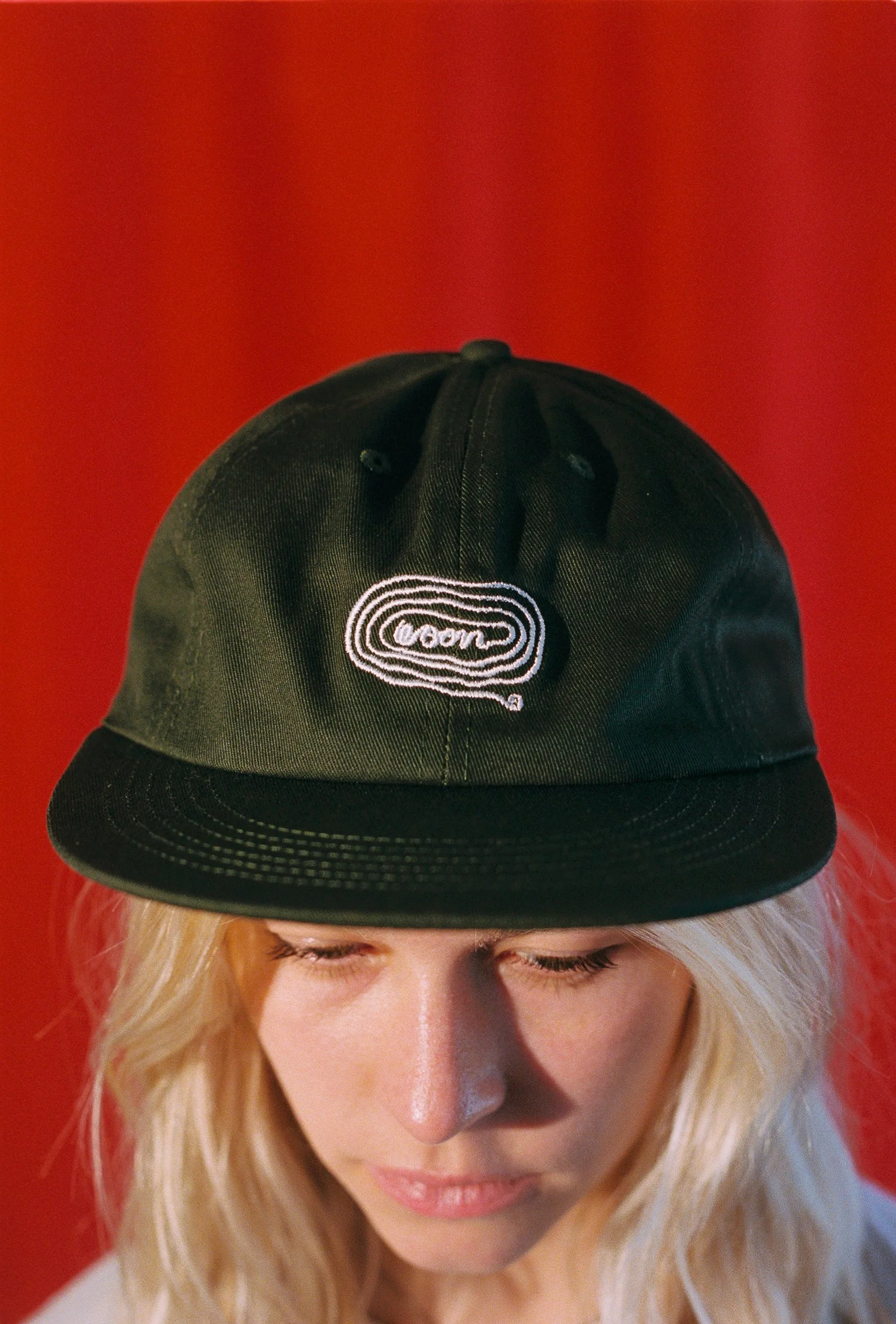 A person wearing a black flat bill cap with white artwork of noodles