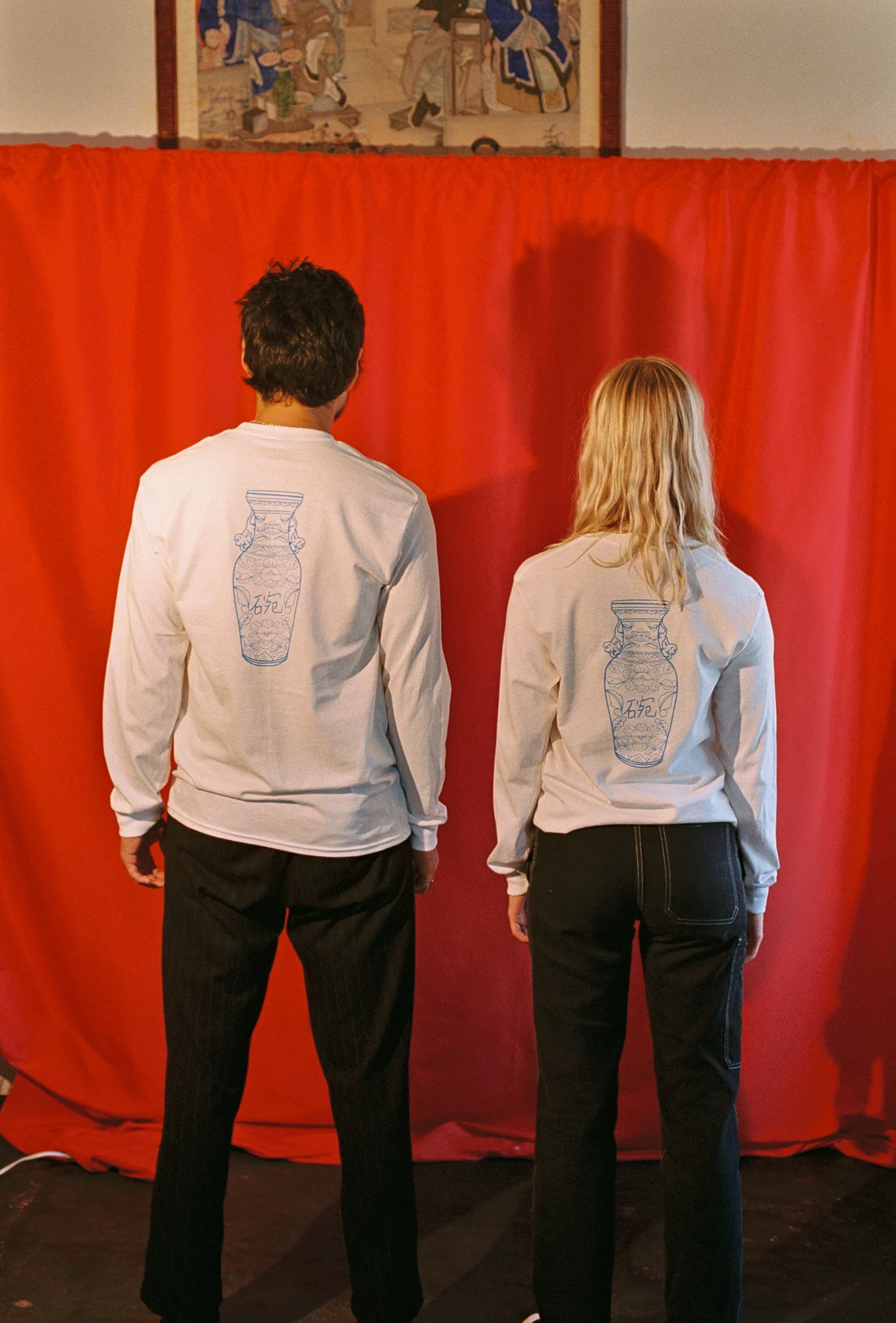 The back of two people wearing white long sleeve shirts with blue artwork of a vase