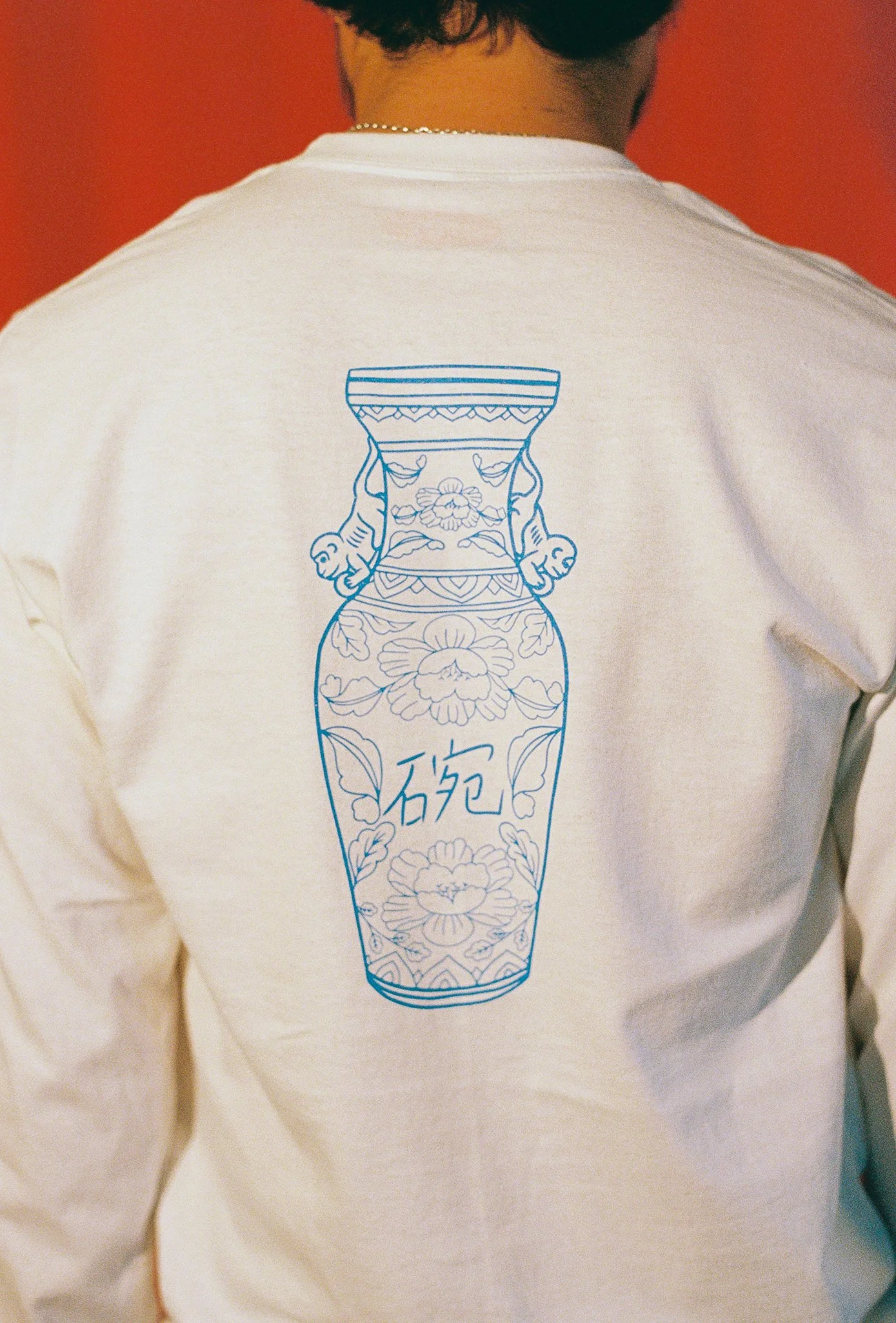 The back of a white long sleeve shirt with blue artwork of a vase