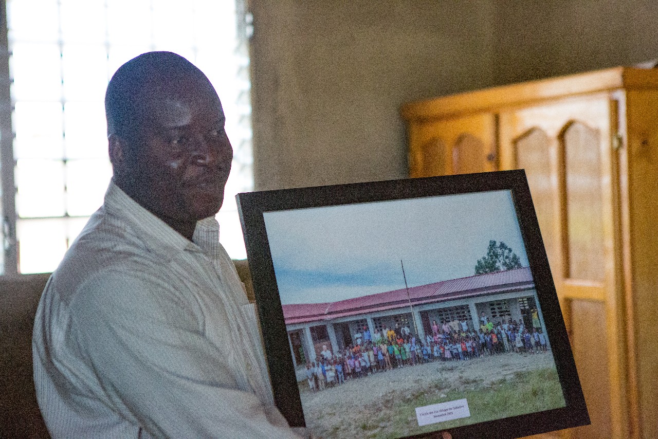 Raymond, the school principal, proudly holds the framed photo of the children of his school taken by our travel group in November 2015 and presented on this trip