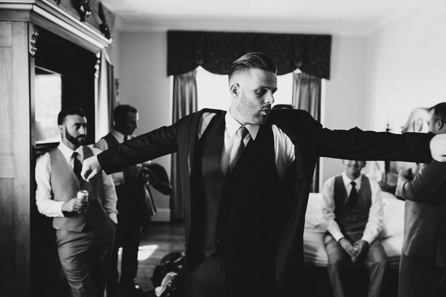 groom surrounded by his groomsmen puts on his jacket at the hote