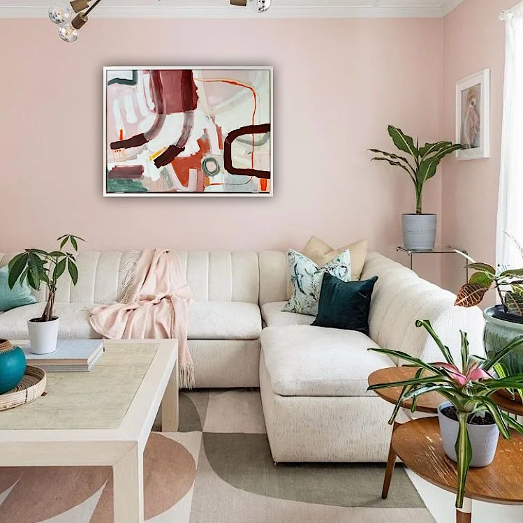 light pink framed abstract painting with brown lines and forms hanging on a cozy pink living room wall