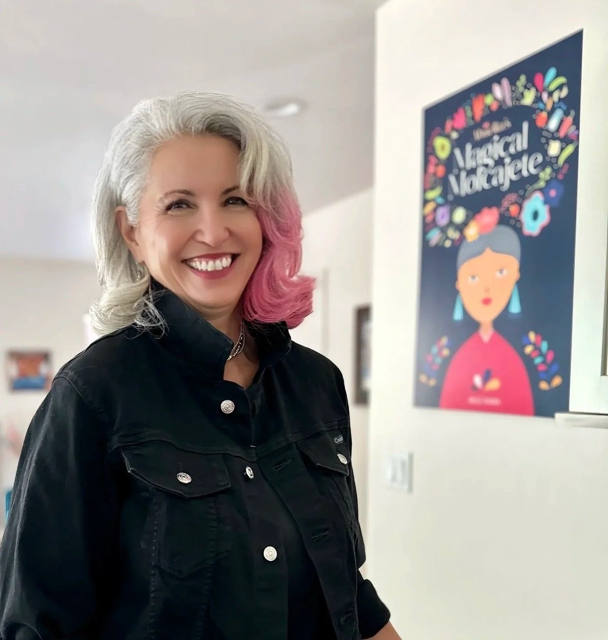Molé Mama standing in her kitchen  next to her Abuelita's Magical Molcajete book cover.