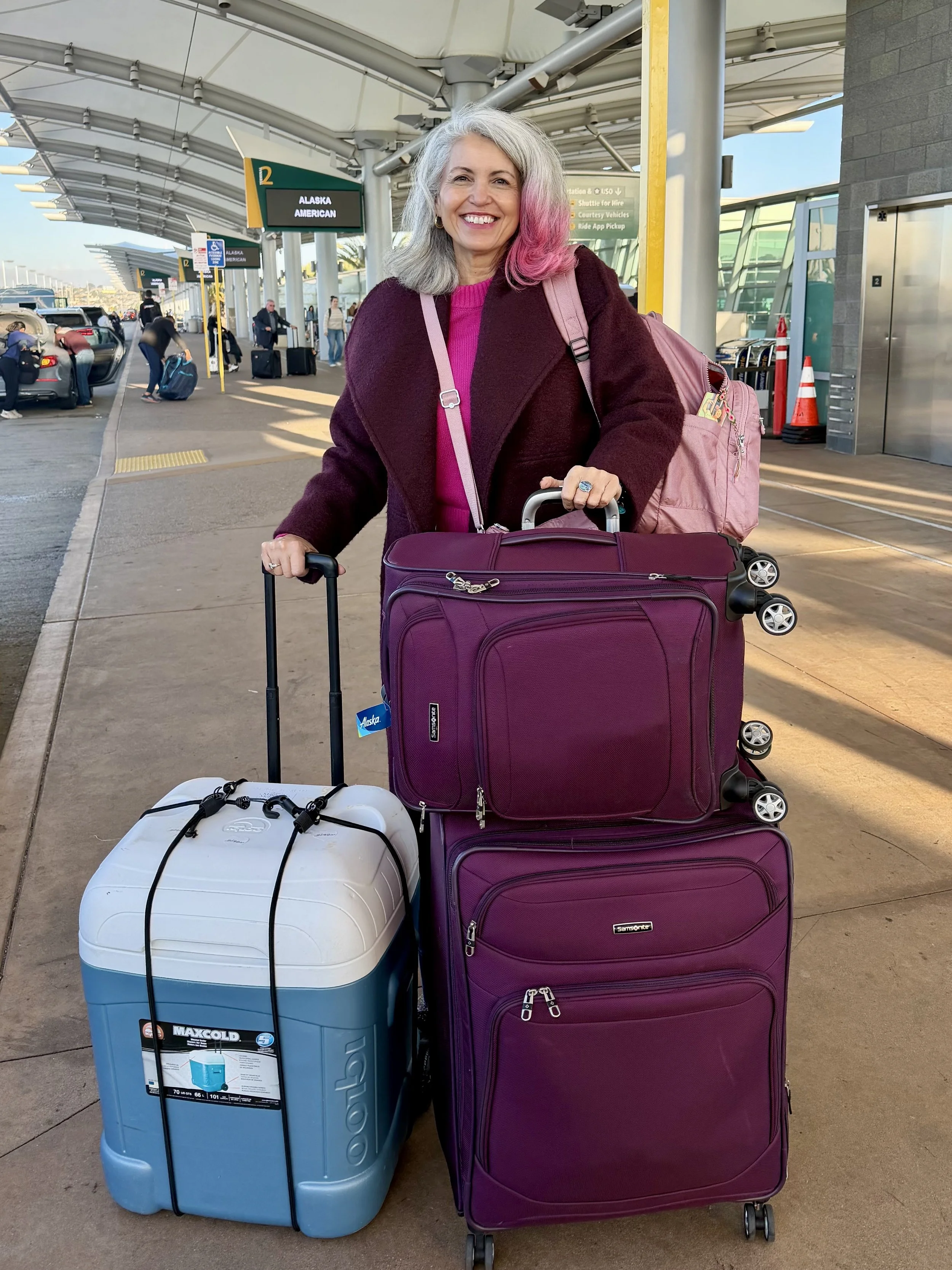 Molé Mama in a long burgundy coat at the airport traveling with a giant white a blue ice chest filled with Mexican food and love